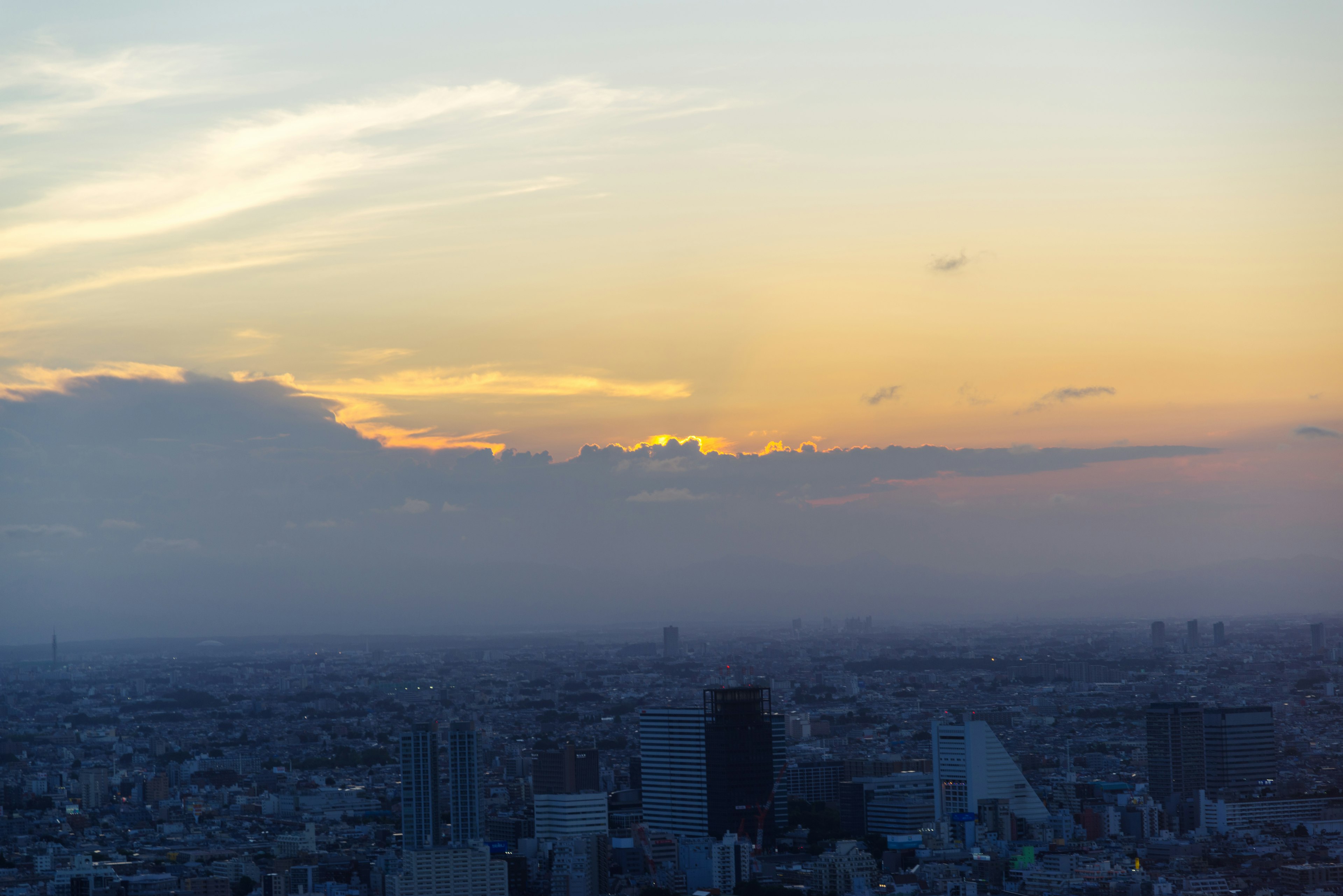 Panorama urbano al tramonto con nuvole e luce arancione nel cielo