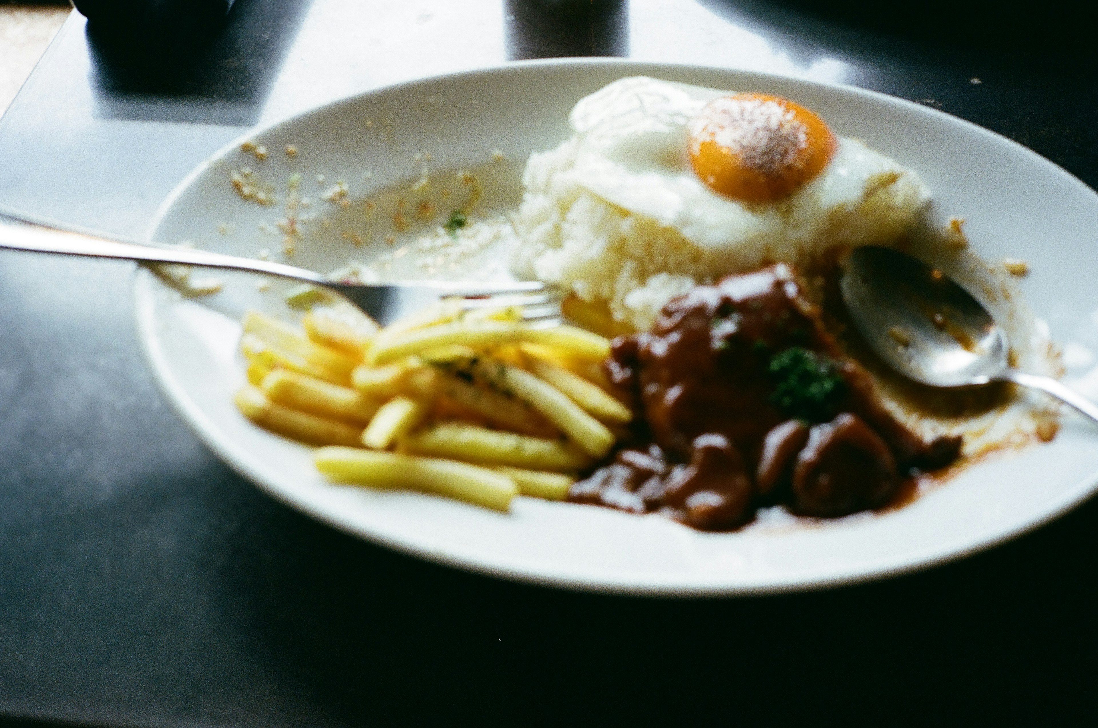 Piring berisi nasi putih dengan telur mata sapi dan hidangan daging berkuah serta kentang goreng