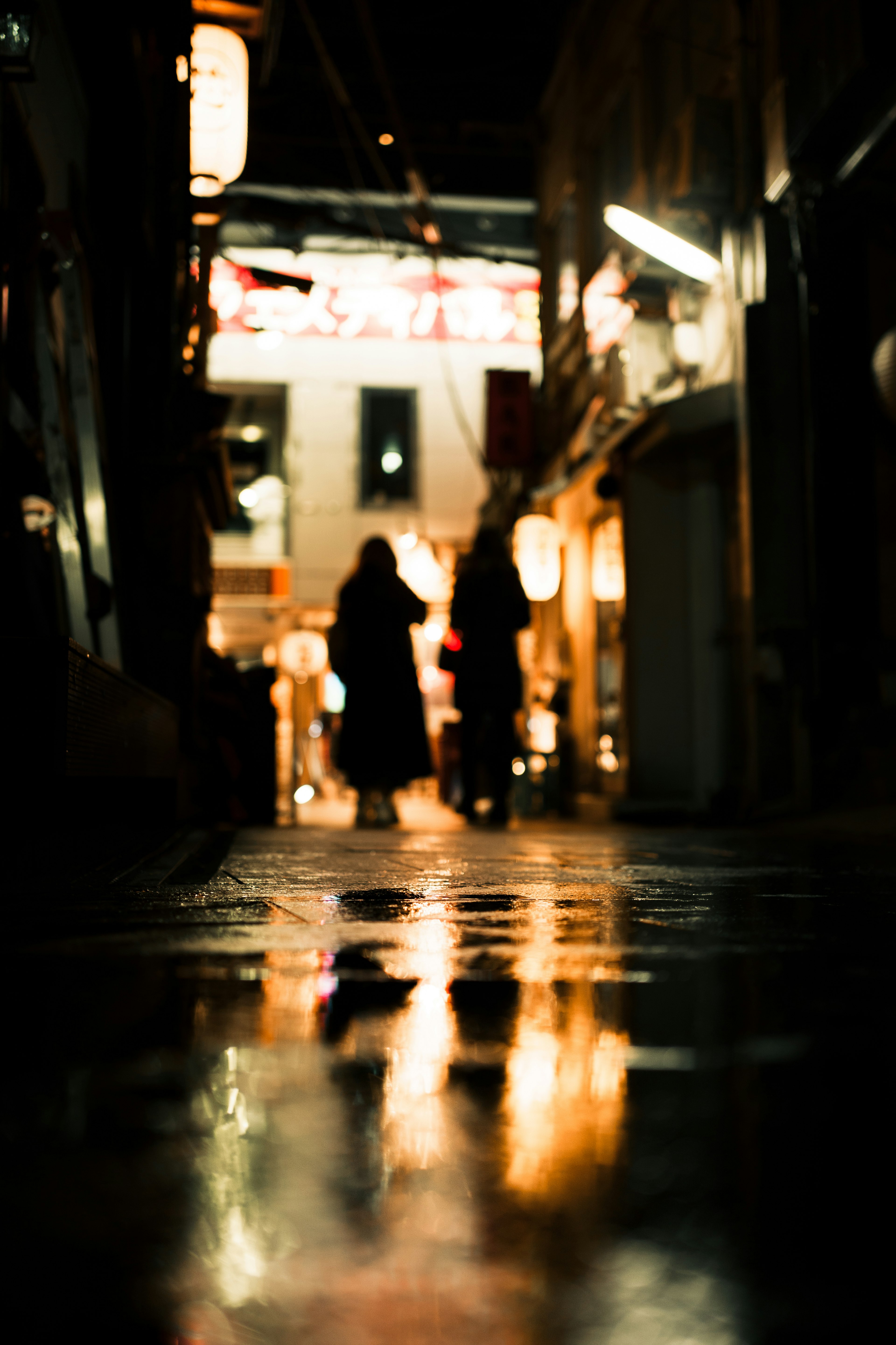 Silhouetten von Menschen in einer nächtlichen Gasse mit Reflexionen auf dem nassen Pflaster