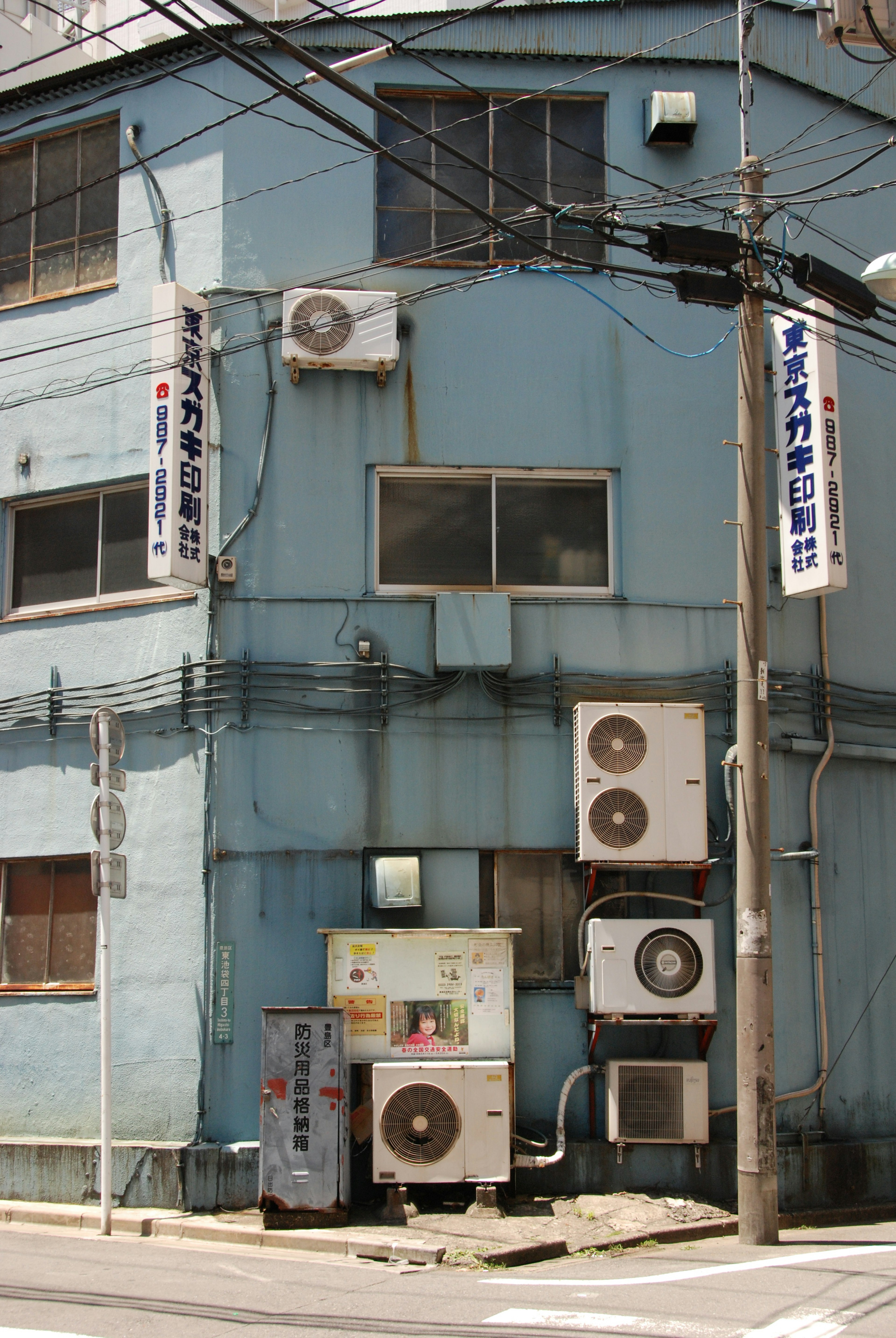 Side of a blue building with mounted air conditioning units and power lines