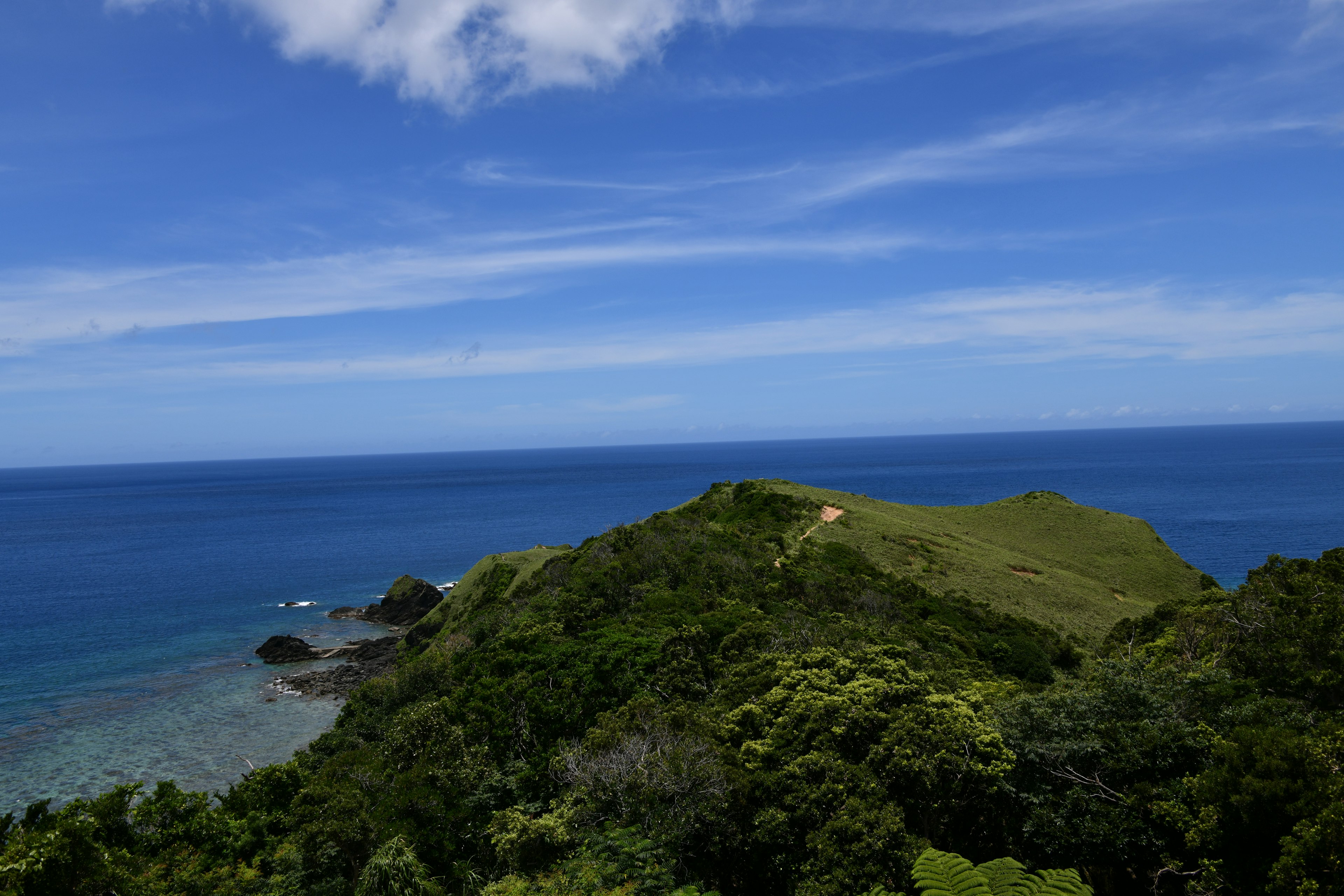 Pemandangan laut biru dan bukit hijau dengan langit cerah dan awan putih