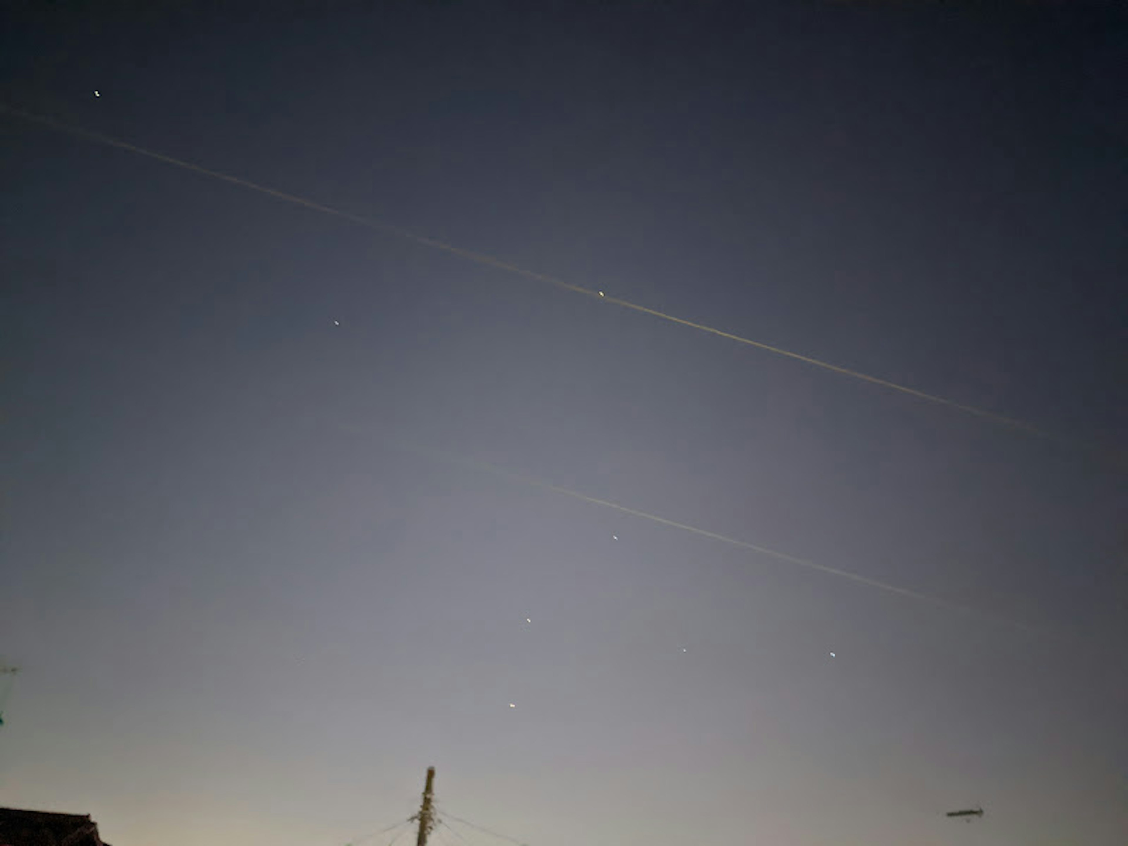 Dunkler Himmel mit verstreuten Sternen und Flugzeugspuren