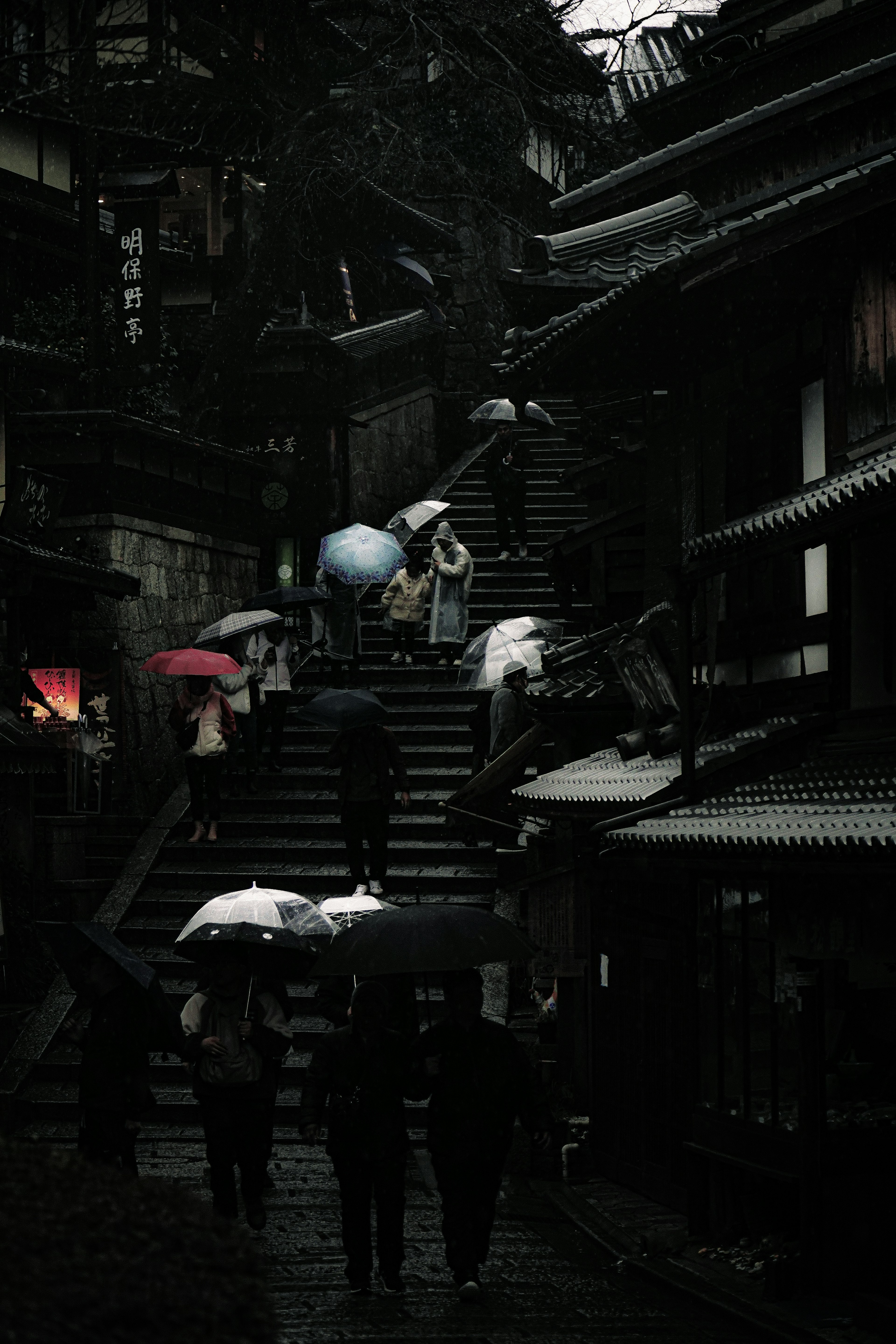 Dark staircase scene with people holding umbrellas in the rain