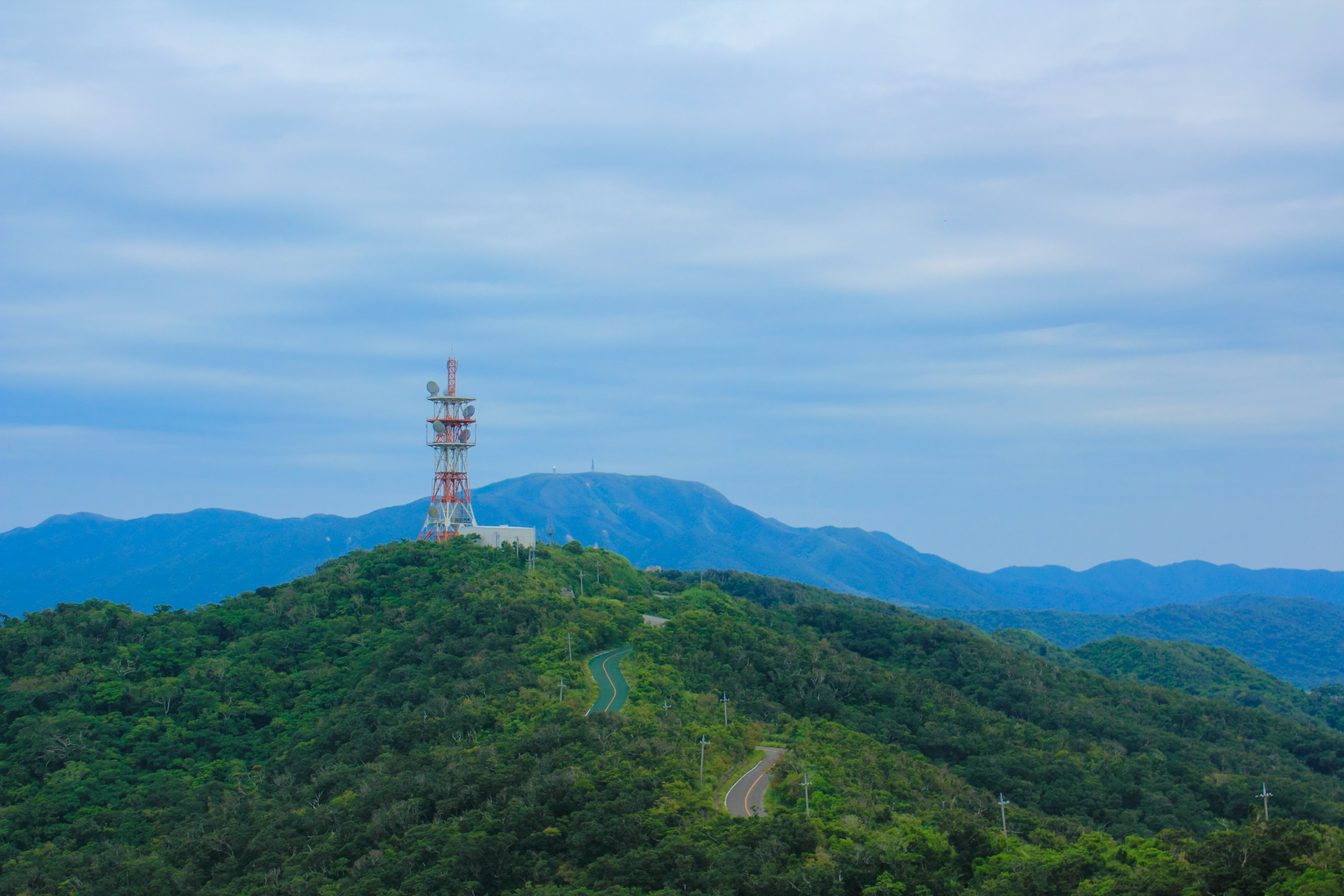 A communication tower on a mountain peak surrounded by green hills