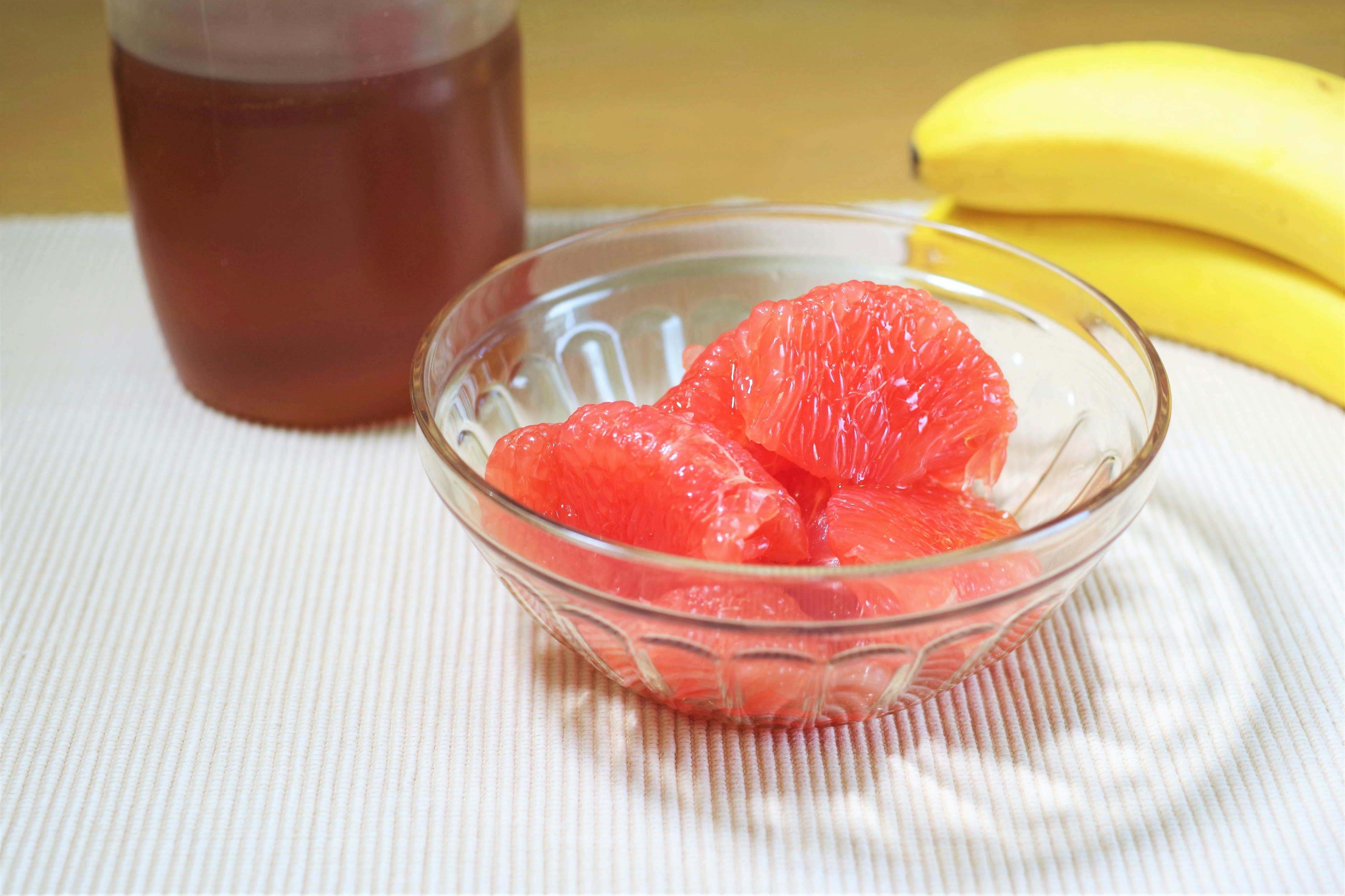 Bowl of pink grapefruit segments next to bananas and a jar of juice