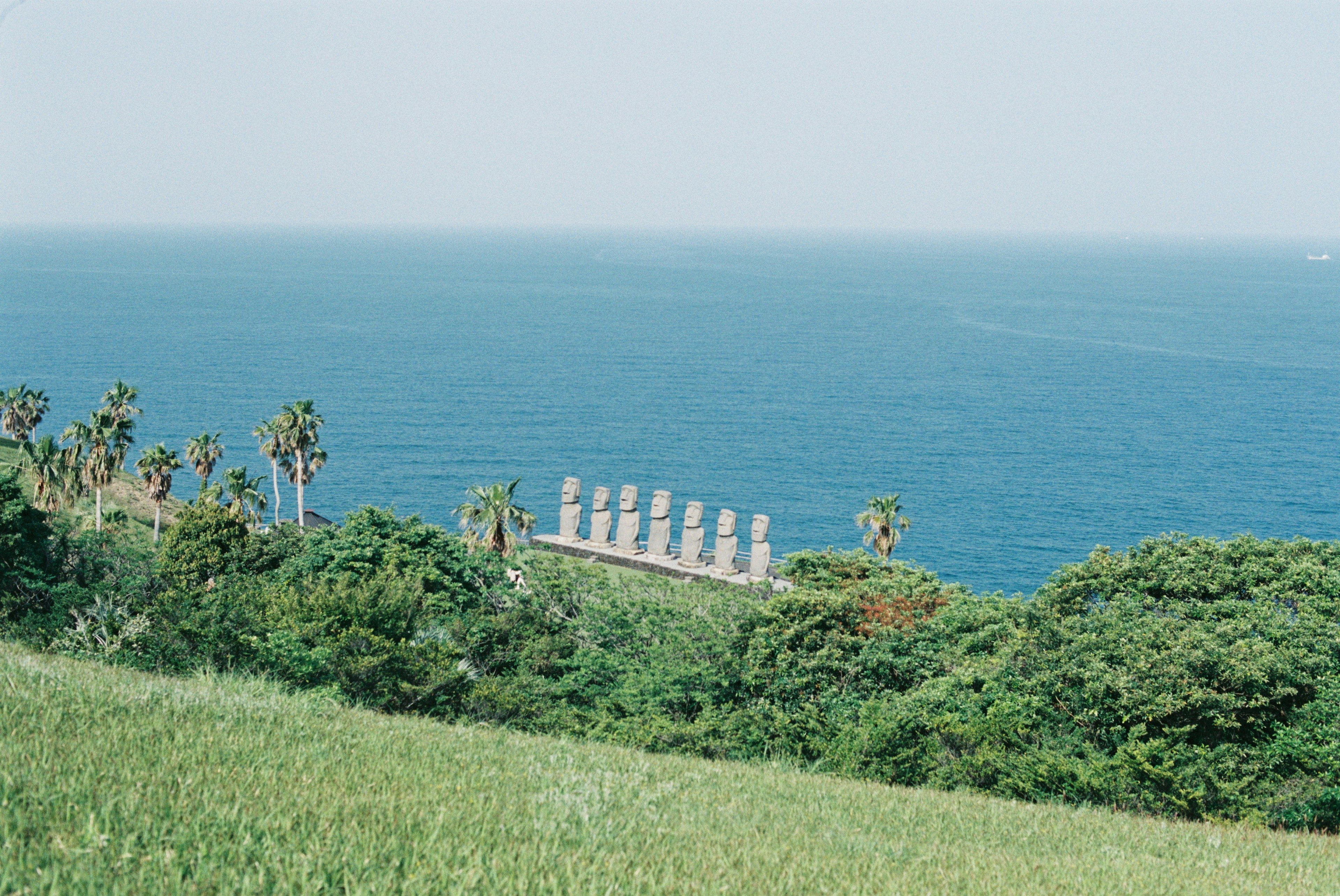 Vue panoramique de statues Moai contre un océan bleu et une colline verte