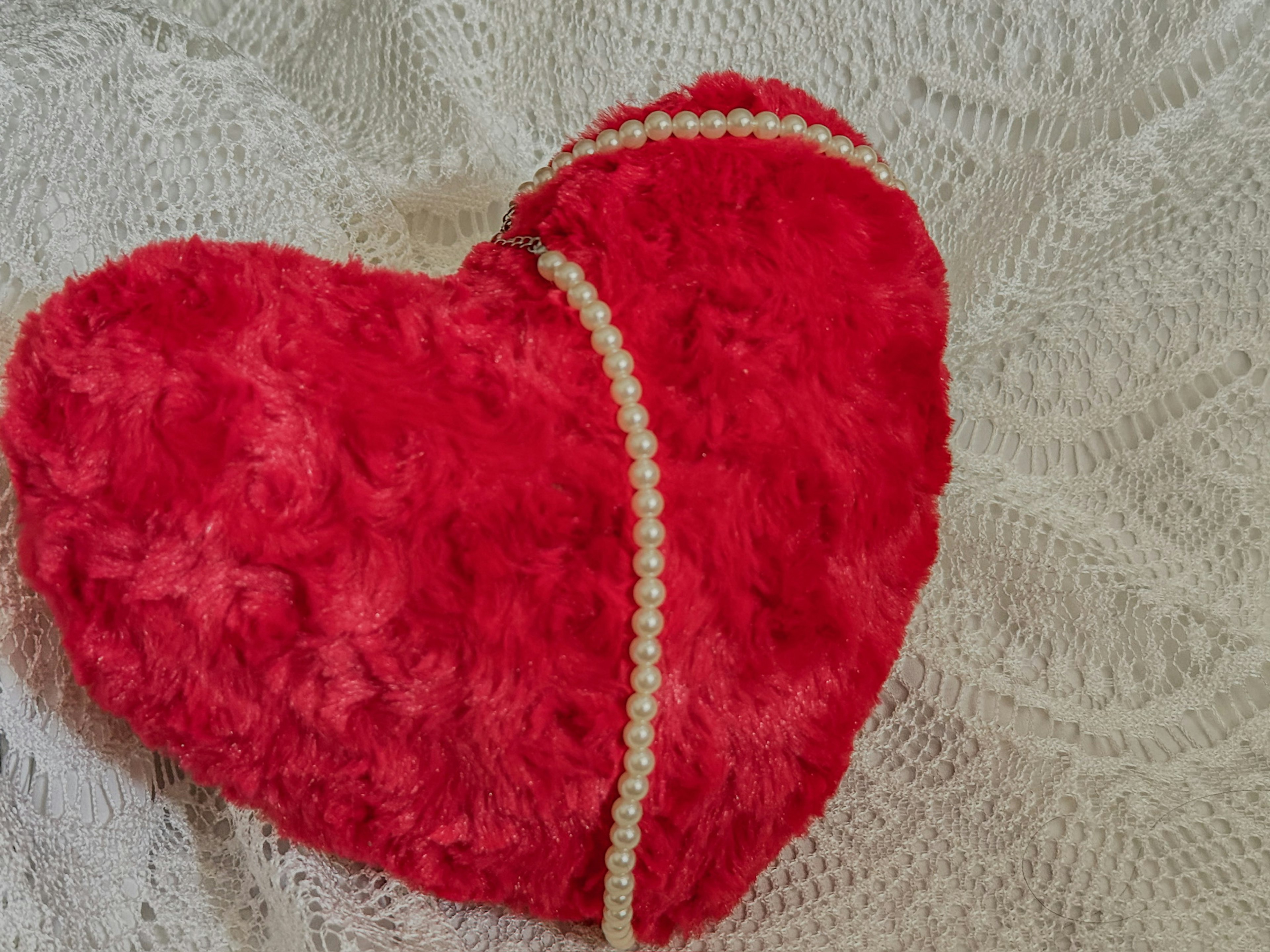 Red heart-shaped cushion with pearl decoration on a lace background