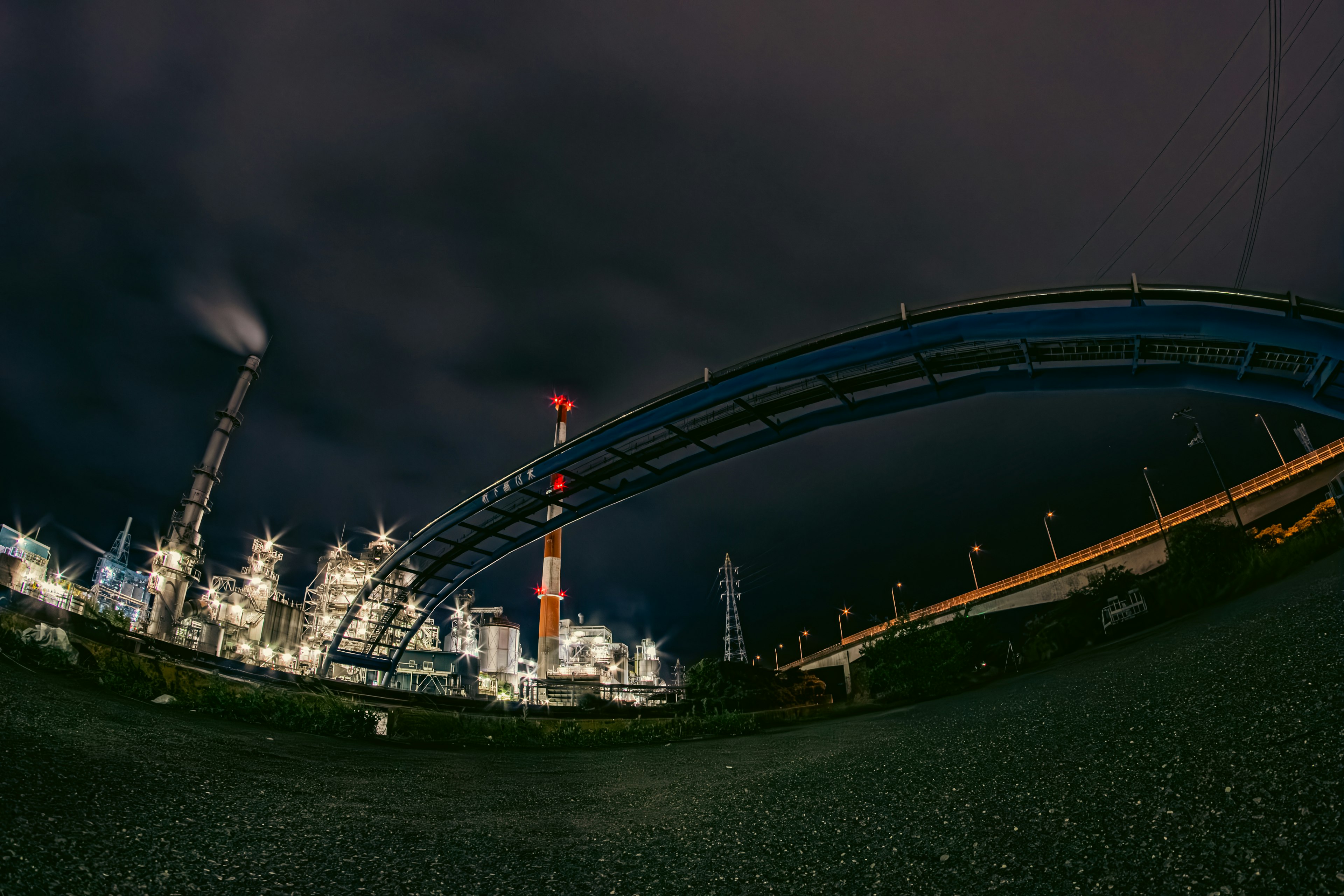 Night industrial scene featuring smokestacks and a blue bridge