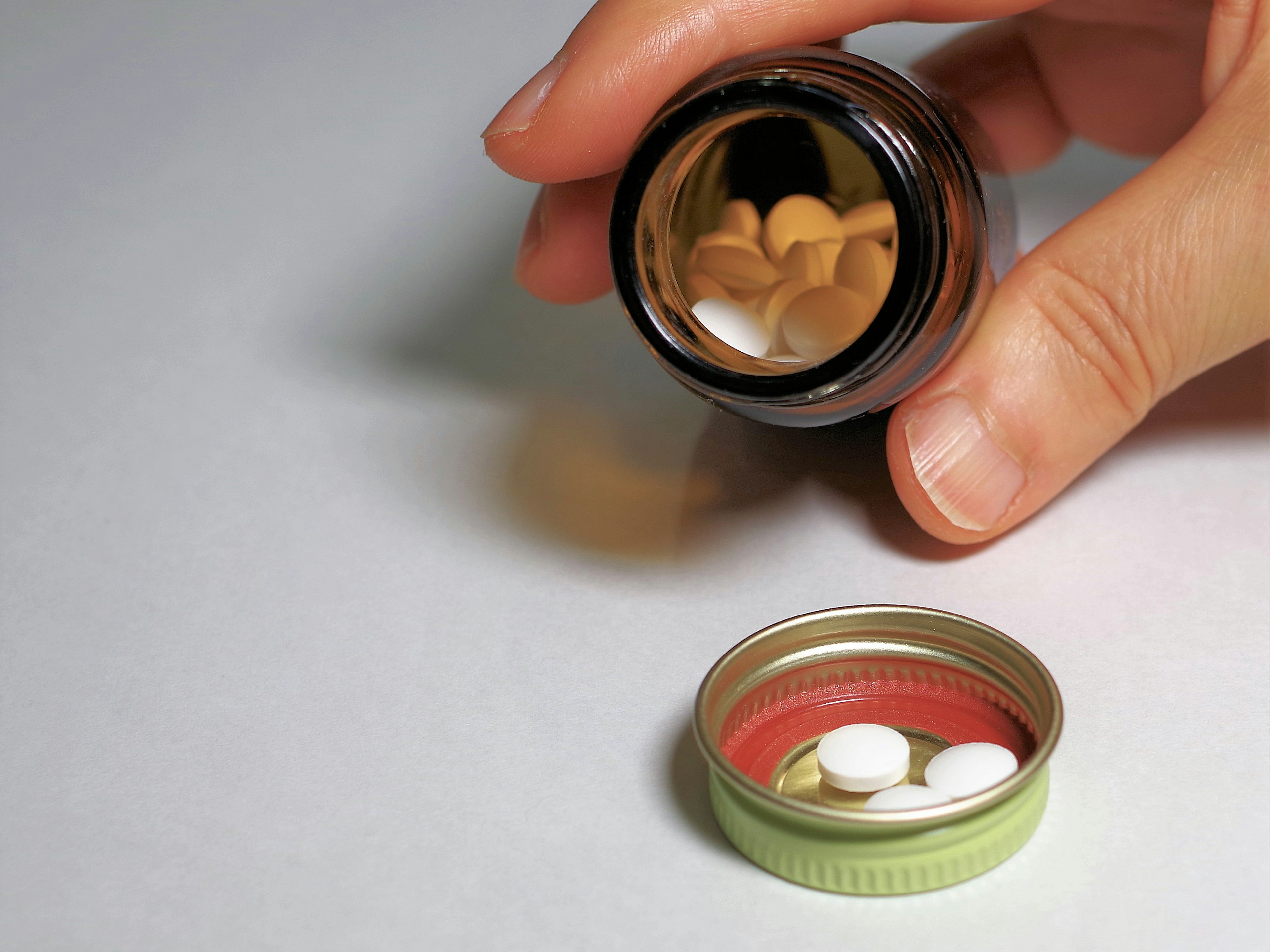 A hand holding a bottle pouring out pills into a container