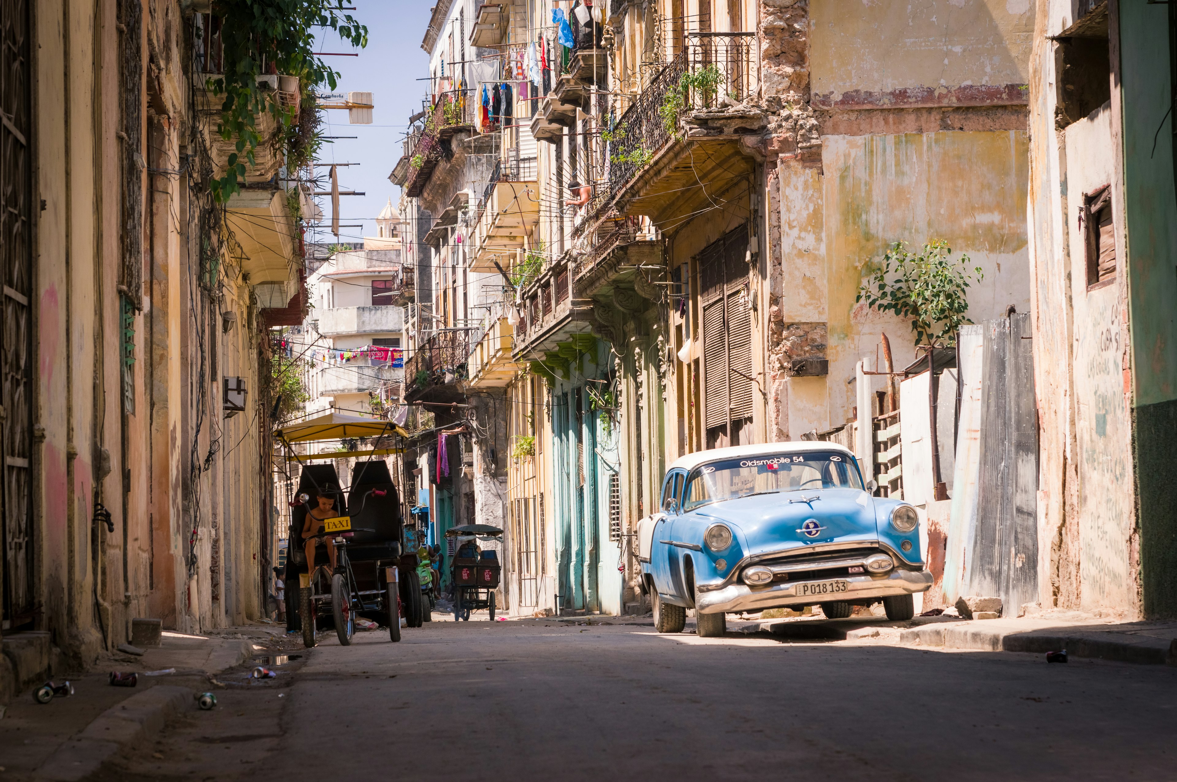 A vintage blue car parked in a narrow street with old buildings