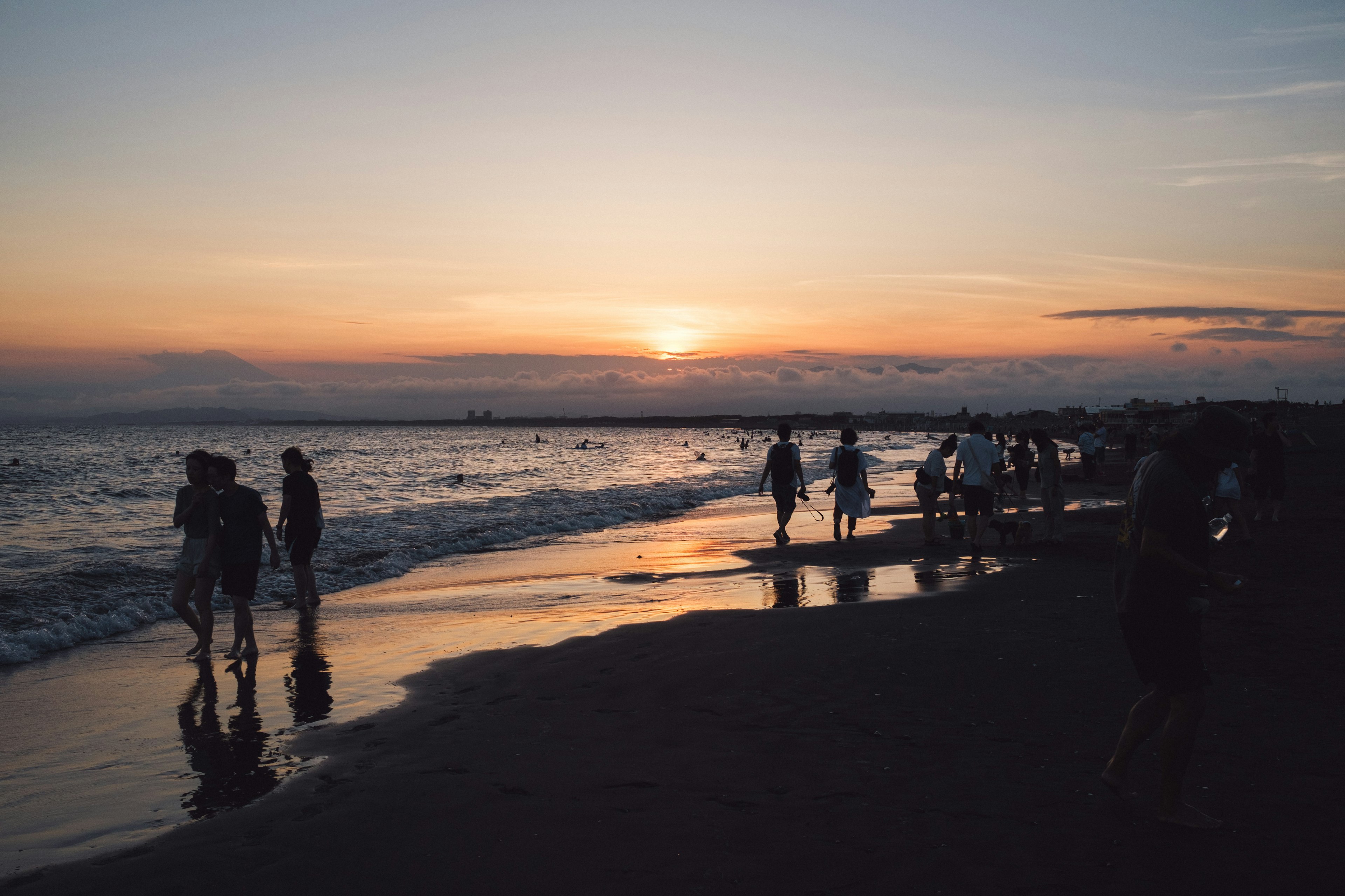 夕日が沈むビーチで散歩する人々のシルエット