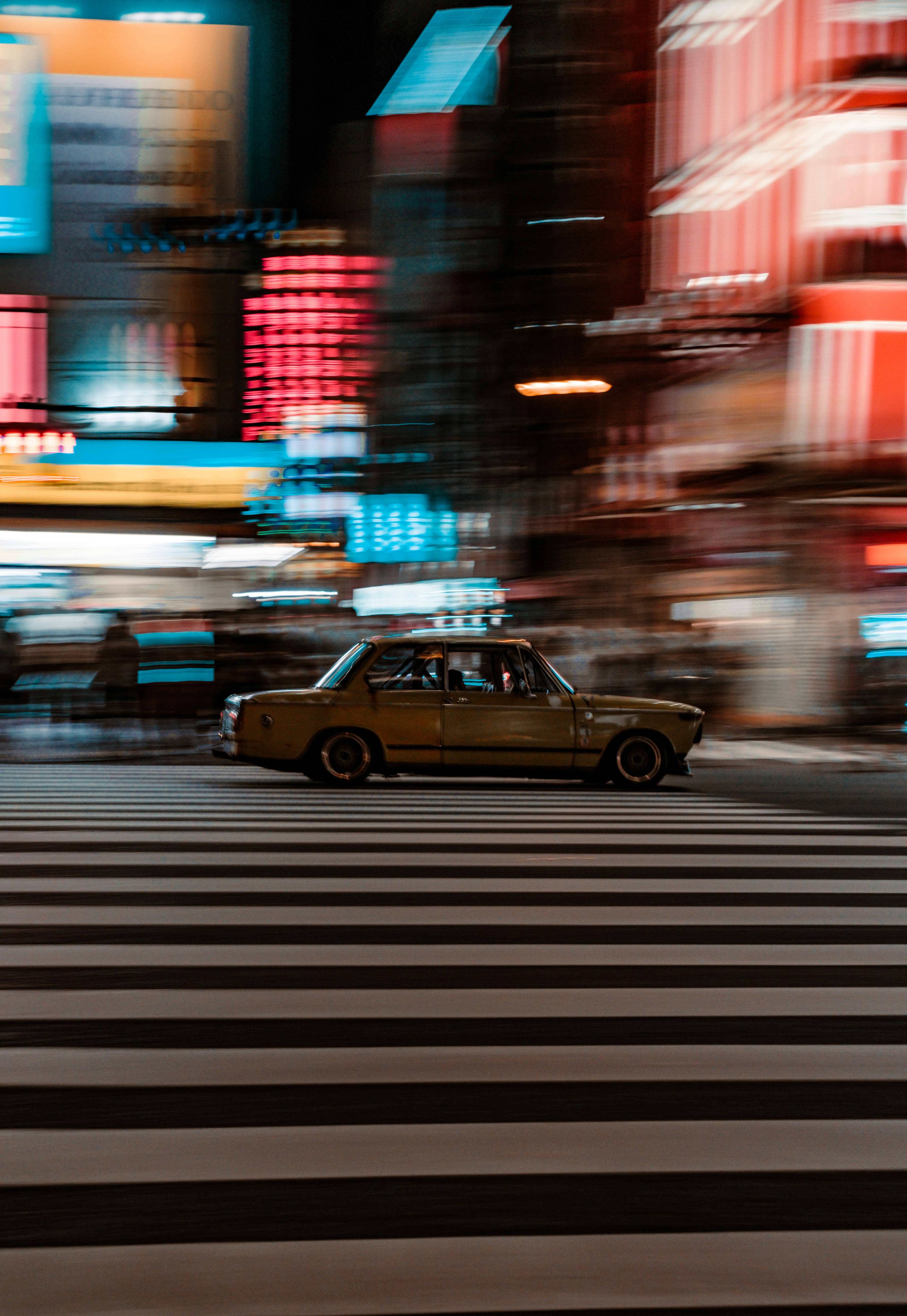 Auto gialla che si muove in una vivace strada cittadina con insegne al neon colorate