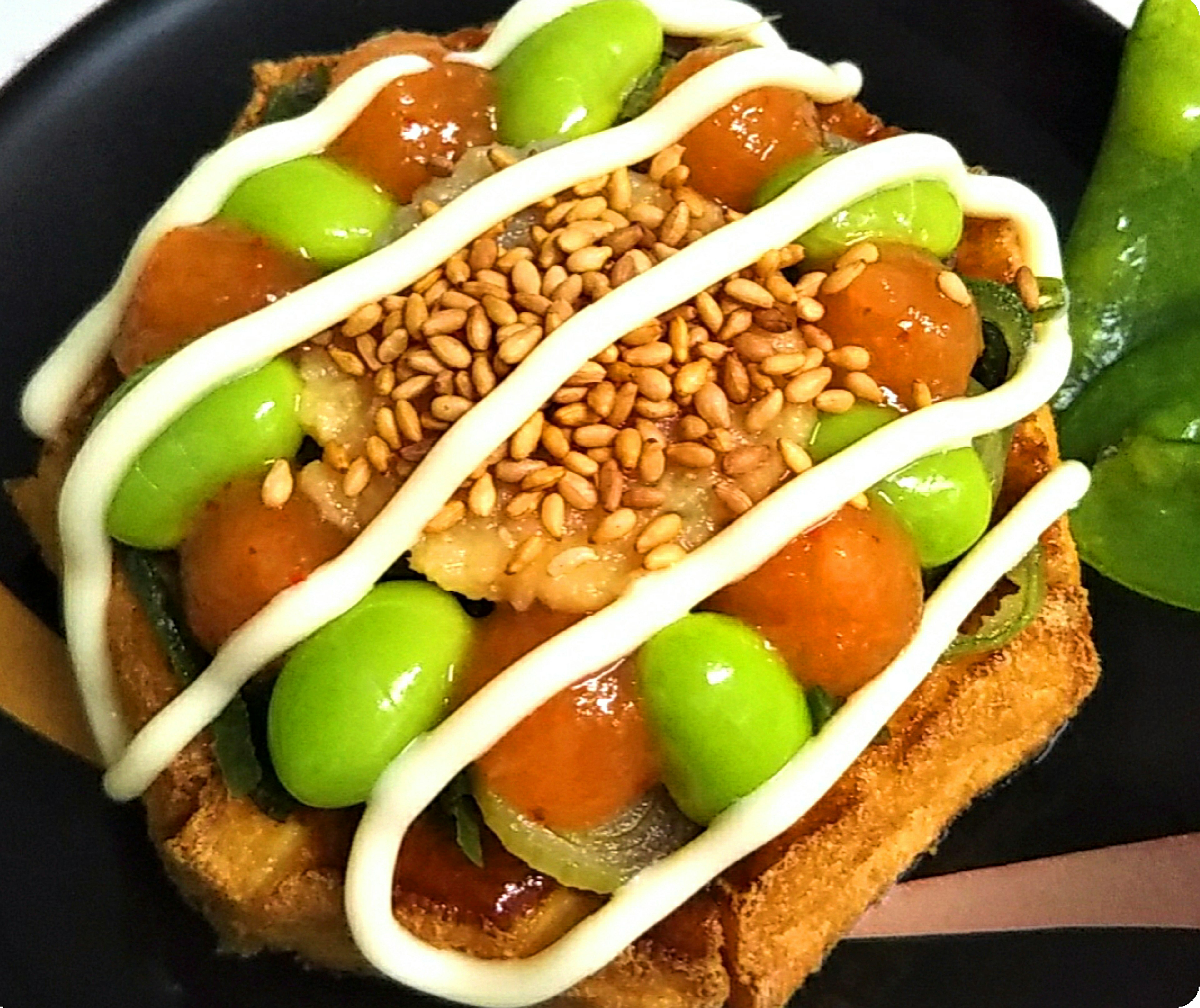 Toast topped with green beans orange sauce white mayonnaise and sesame seeds on a black plate