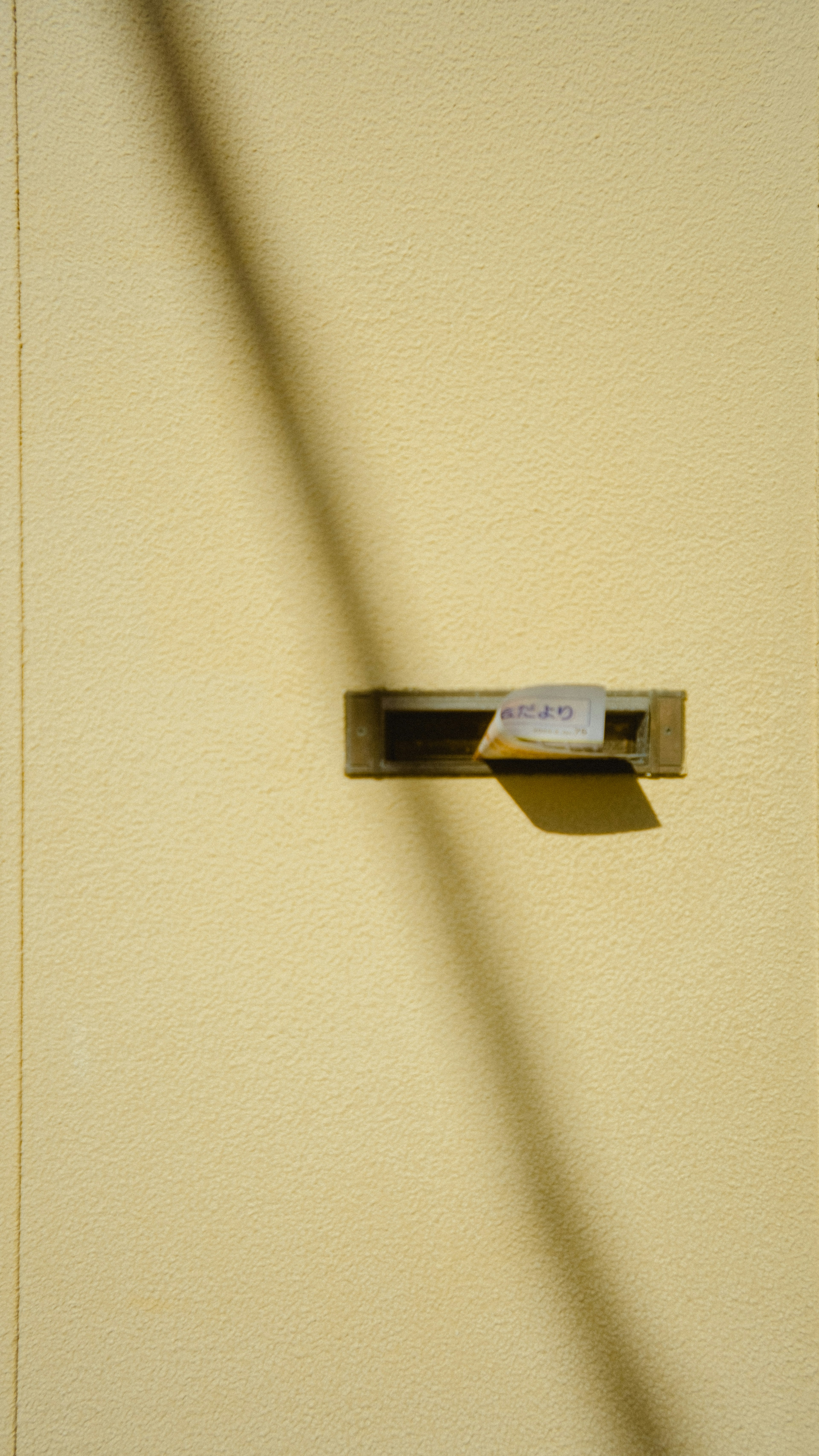 Schlanker Briefkasten an einer gelben Wand mit einem geworfenen Schatten