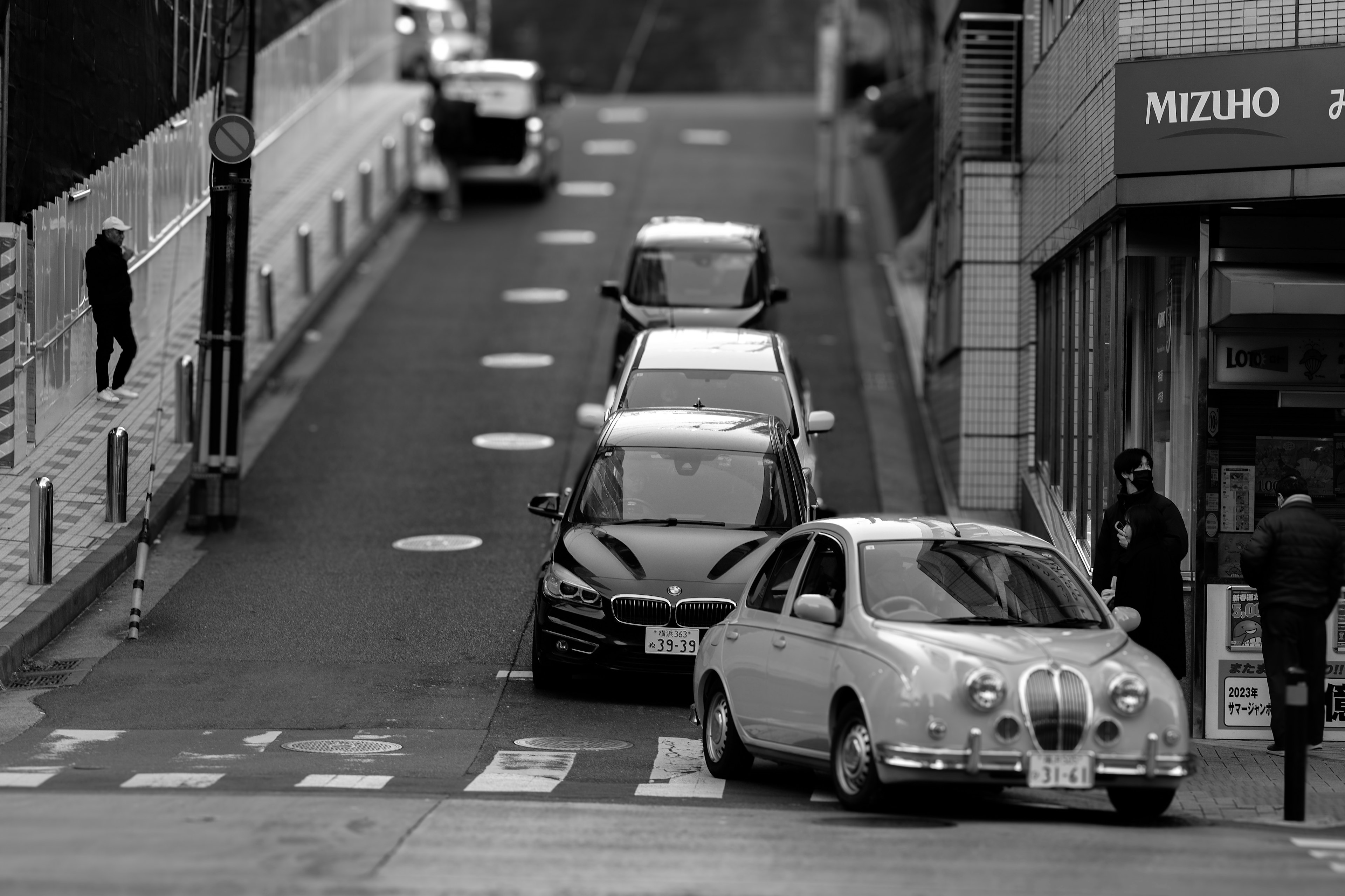 白黒の街並みで停車している車両群と歩行者