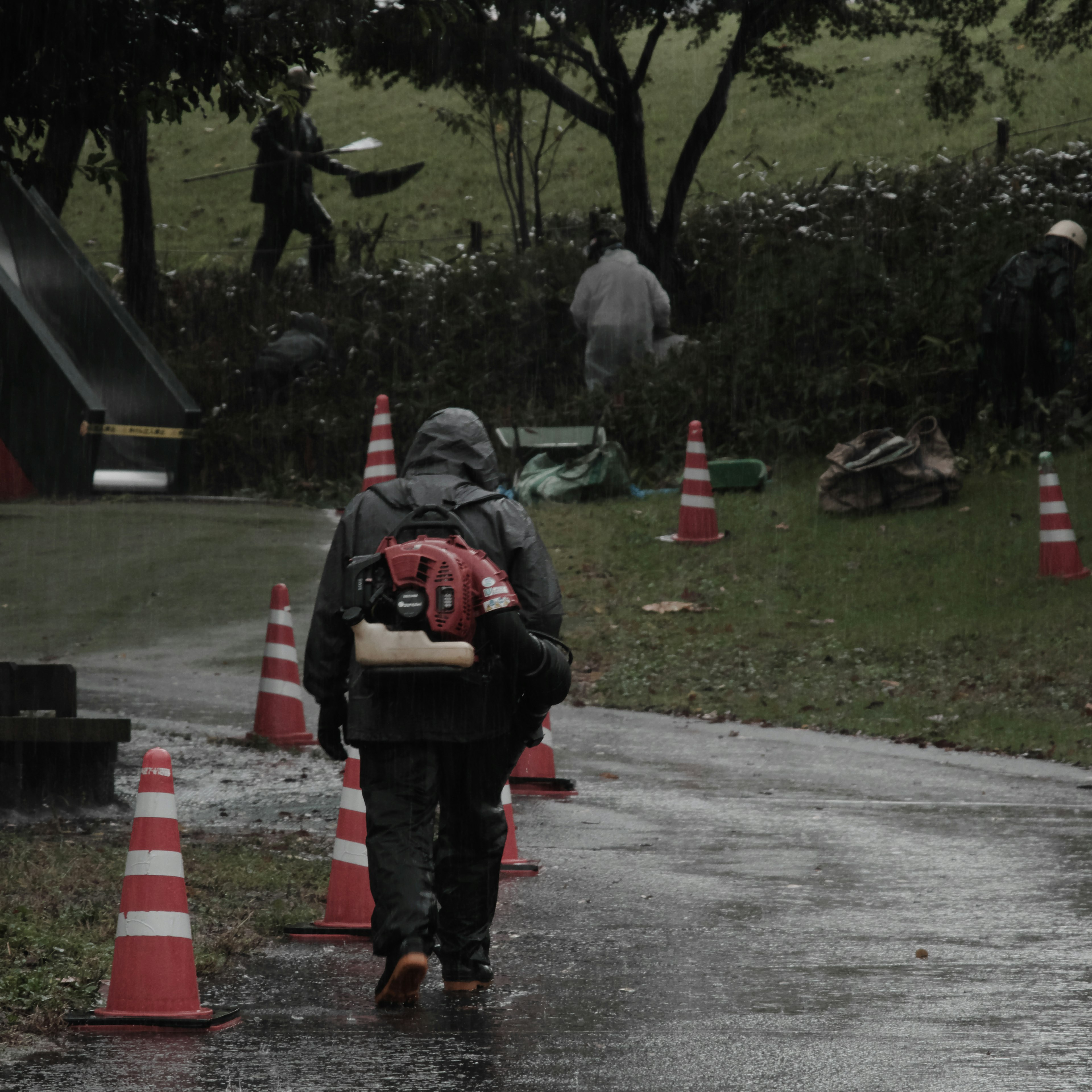 Travailleurs en équipement de pluie effectuant des tâches avec des cônes de circulation dans un environnement humide