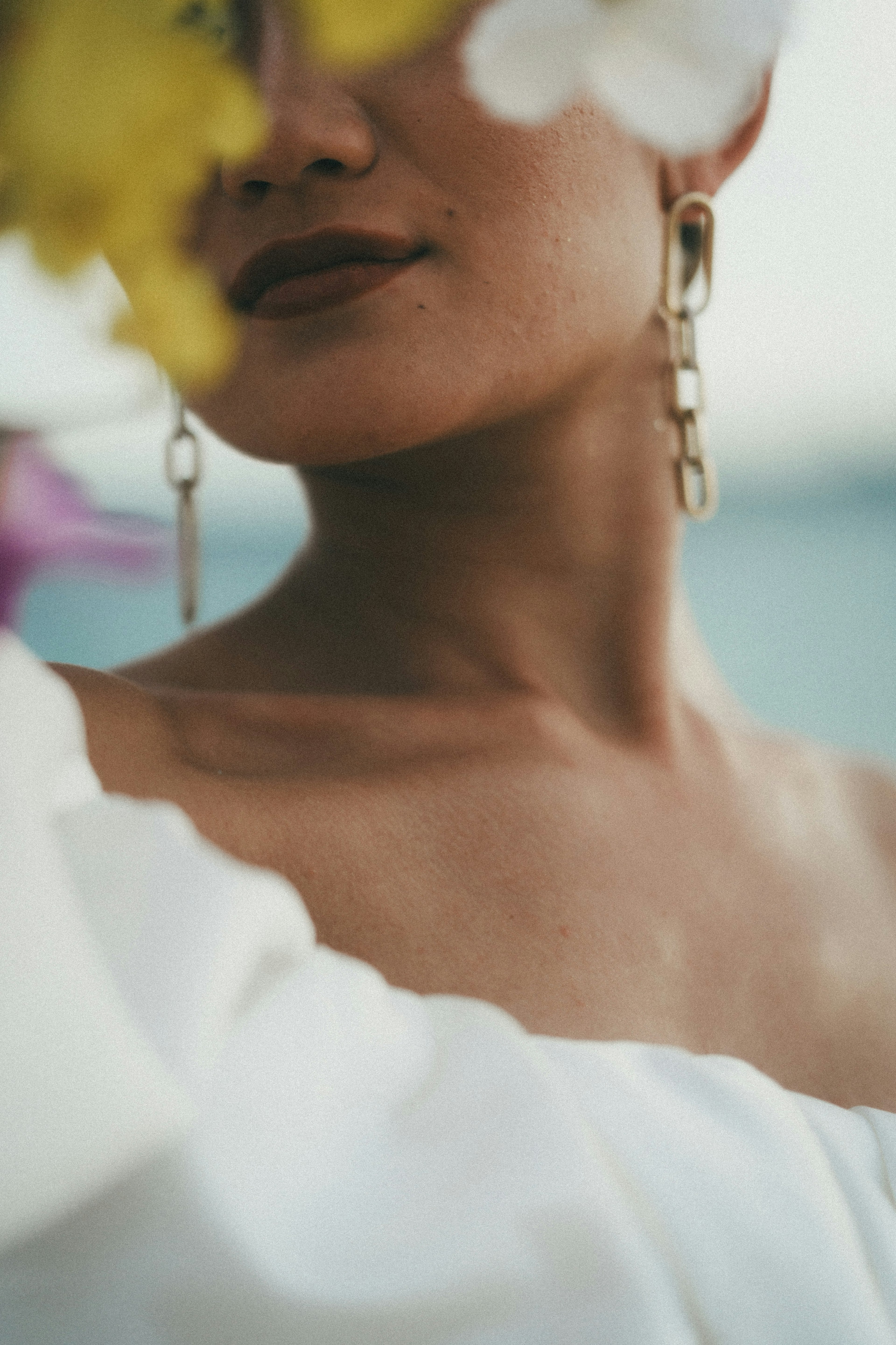 白い服を着た女性の肩と顔の一部が見える写真 色とりどりの花が背景にある