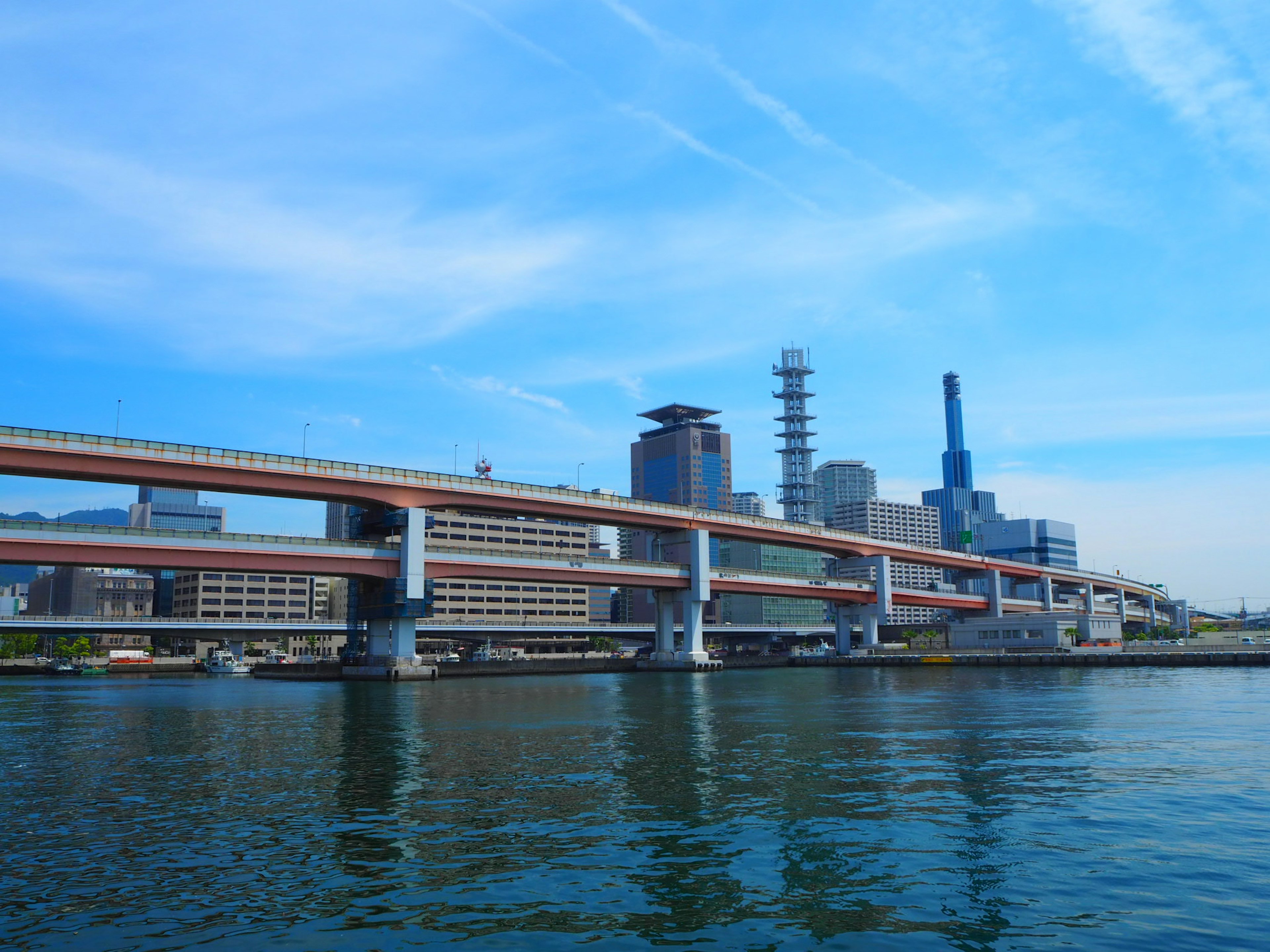 Urban landscape under blue sky featuring a highway and buildings reflecting on the water