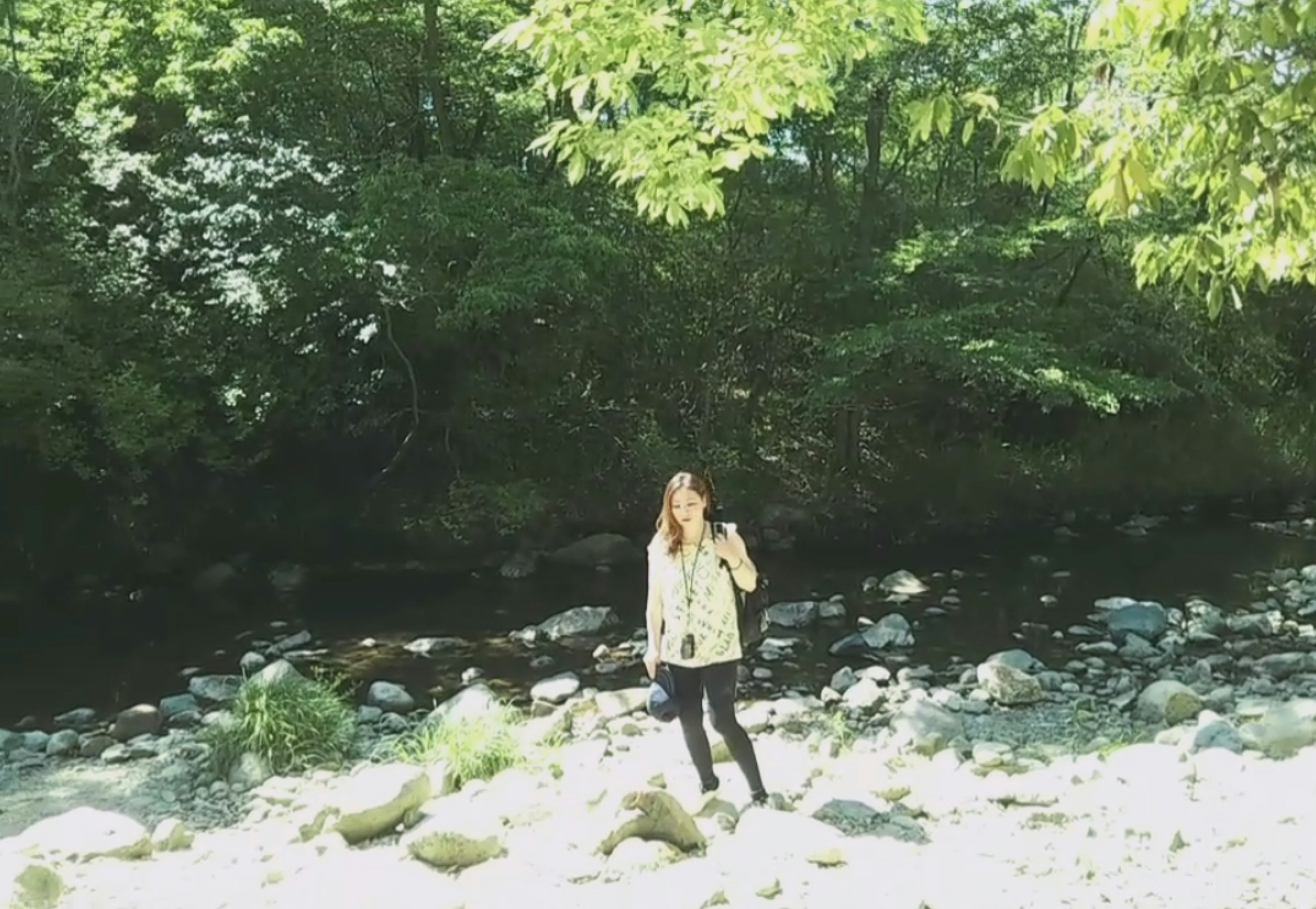 Woman standing by a riverbank surrounded by greenery