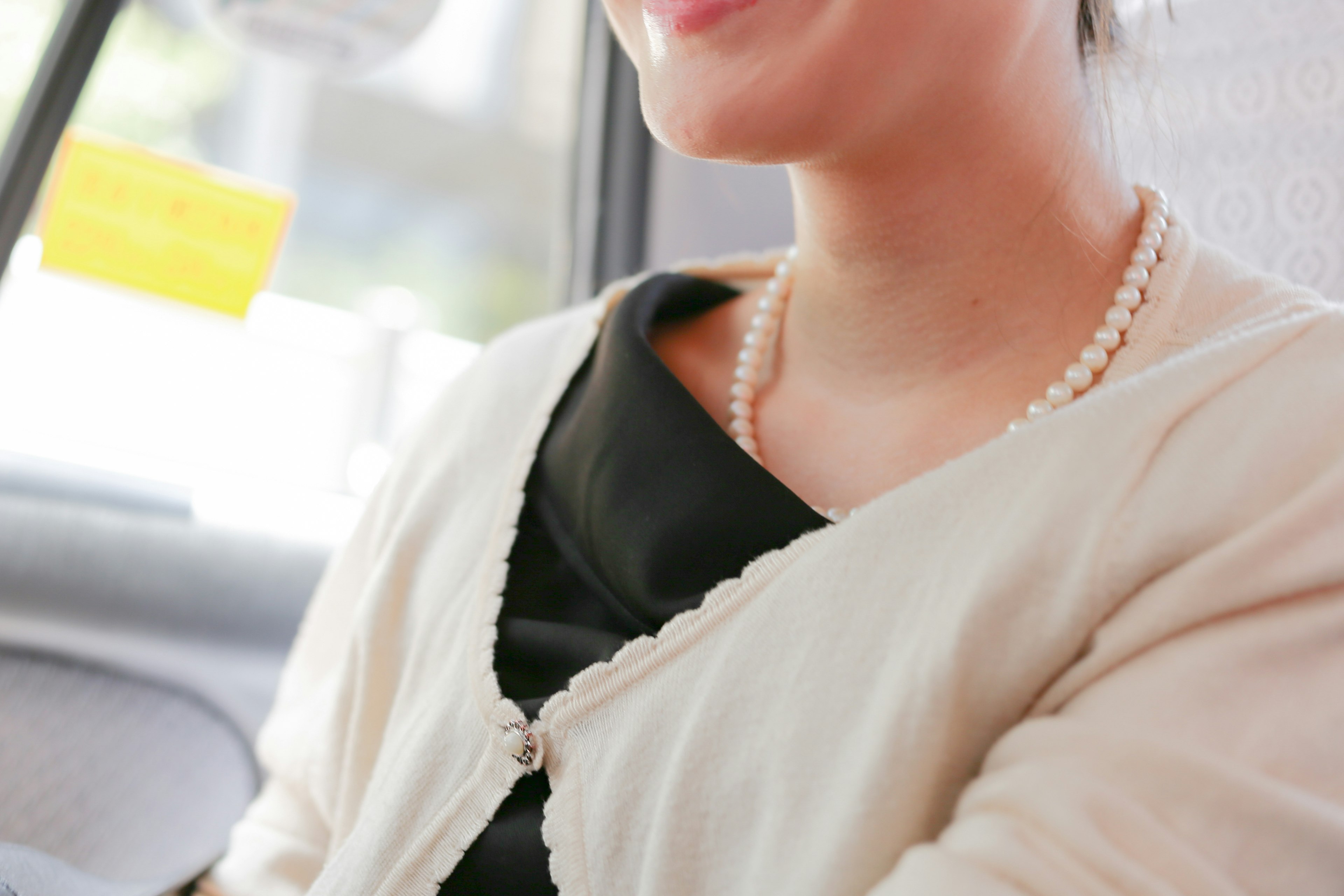 Gros plan sur une femme souriante dans un taxi portant une tenue noire et un collier de perles