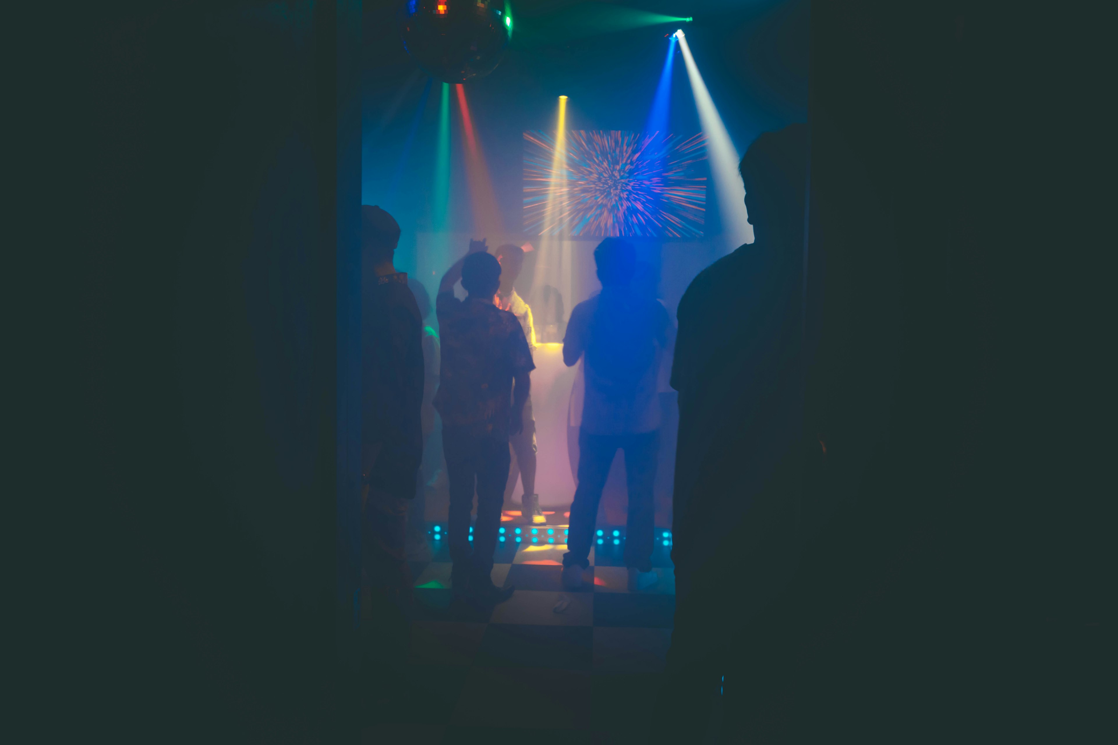 Silhouetted figures in a dimly lit space with colorful lights in the background