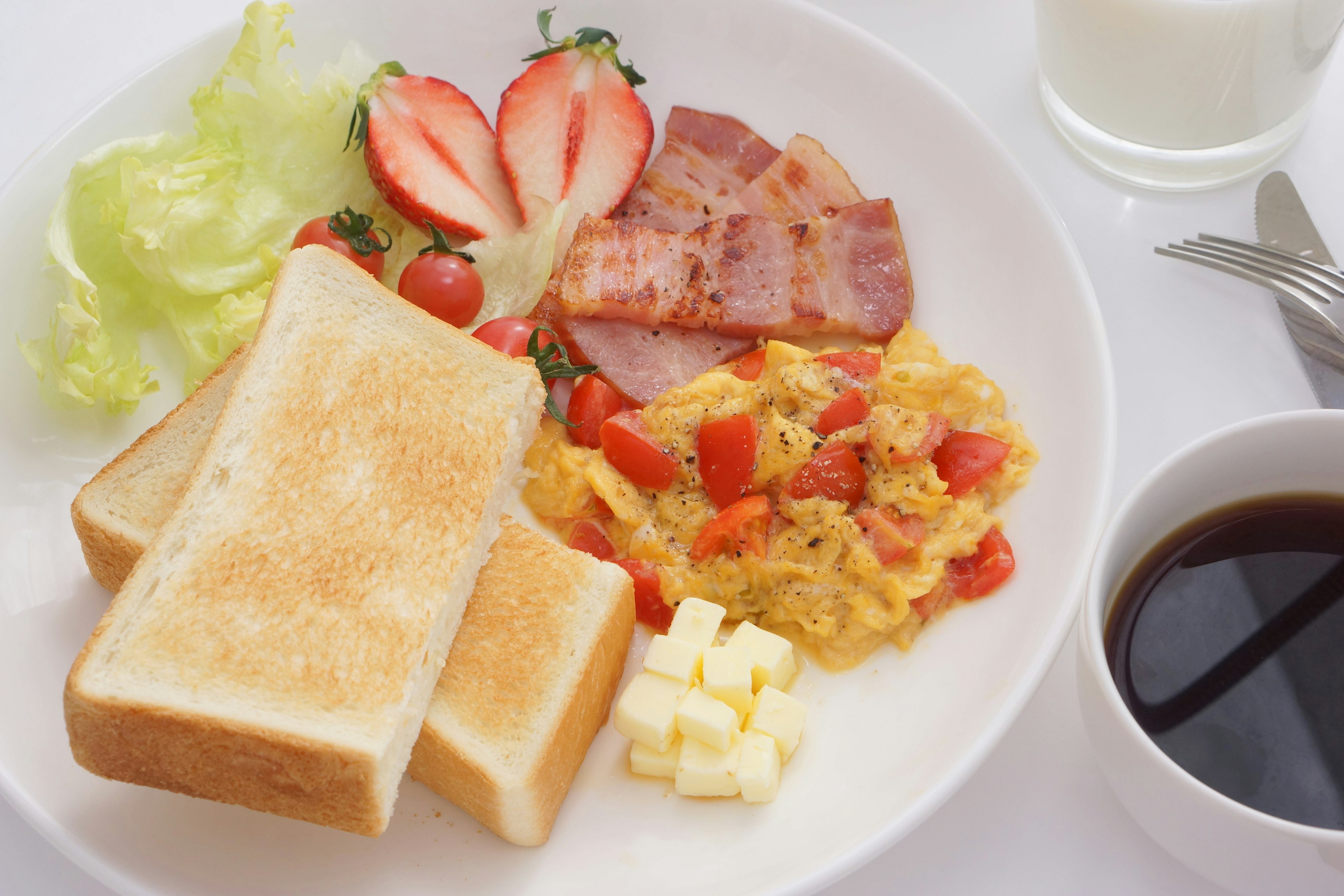 Breakfast plate featuring toast scrambled eggs bacon tomatoes lettuce strawberries and butter