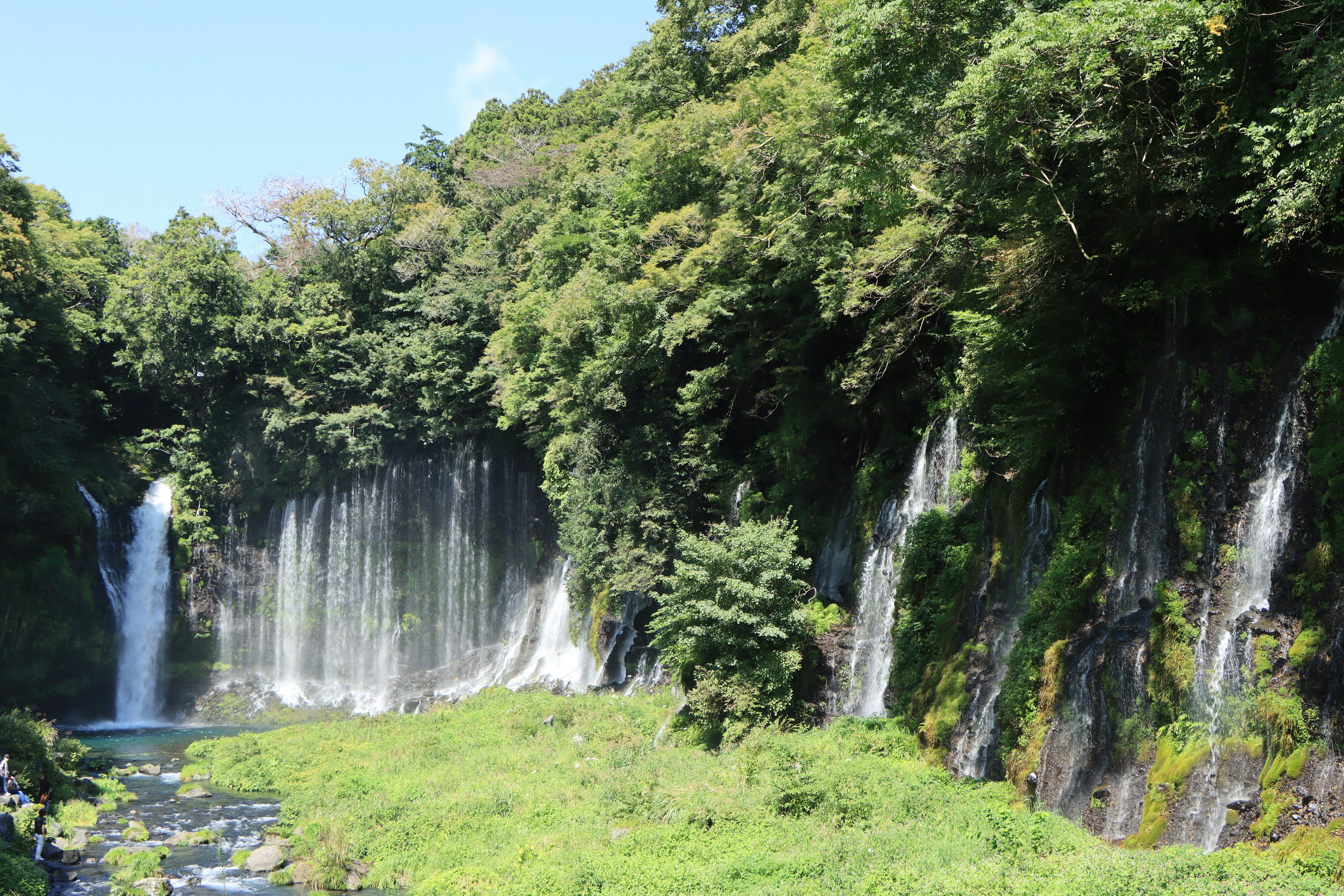 Pemandangan air terjun yang dikelilingi oleh hijauan subur di bawah langit biru