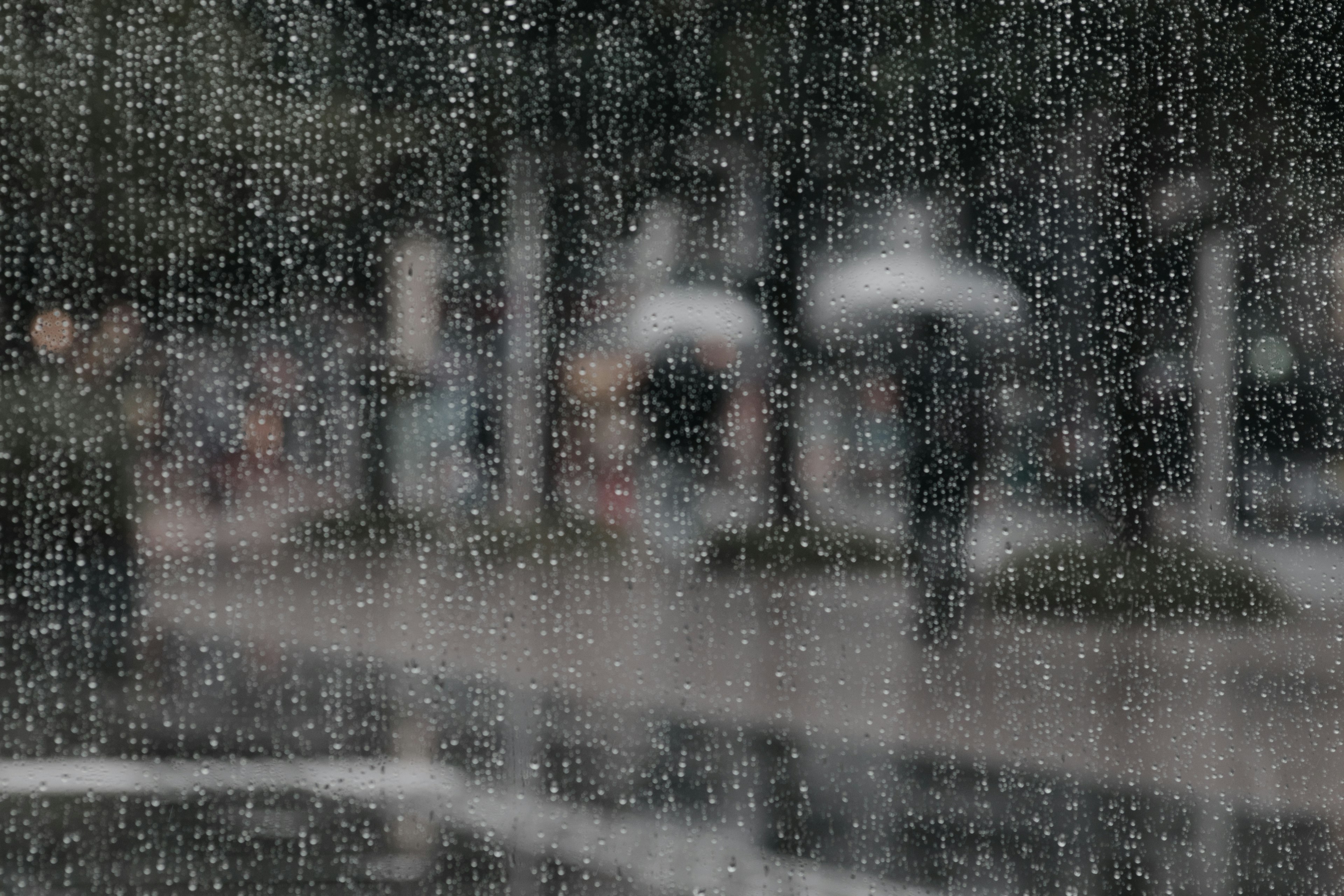 Menschen, die bei Regen mit Regenschirmen gehen, durch ein nasses Fenster gesehen