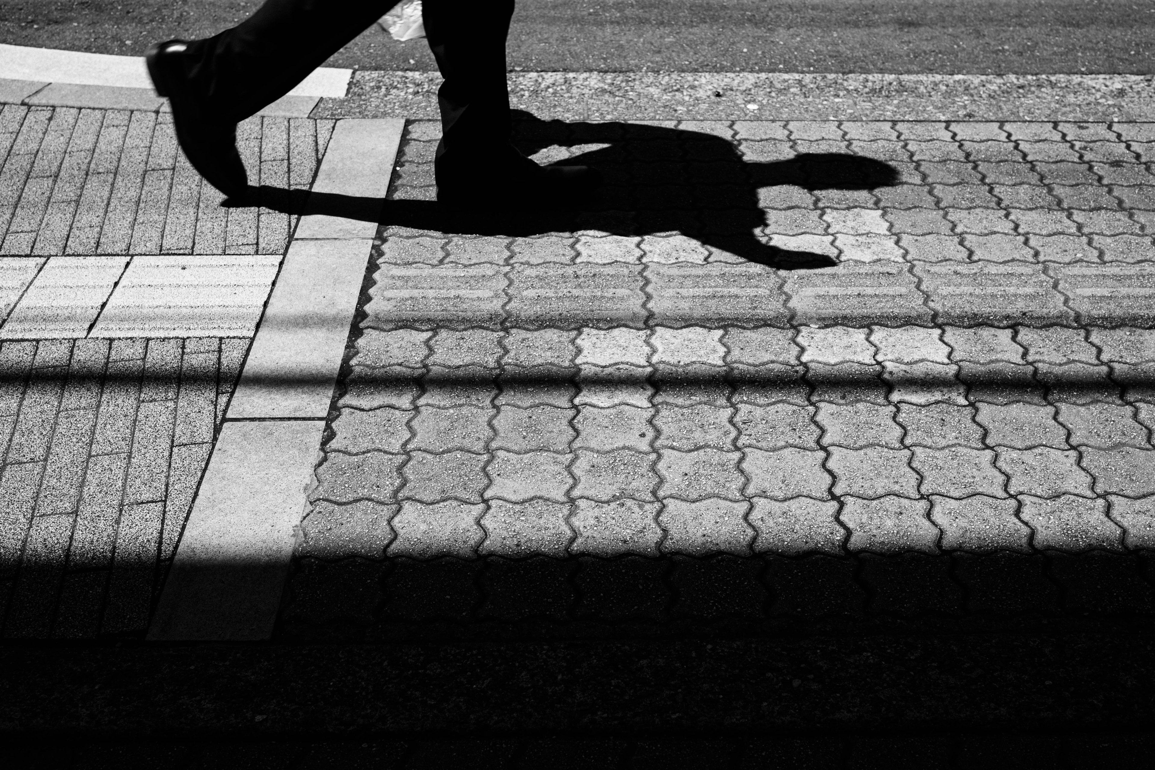 A shadow of a person walking on a patterned pavement in monochrome