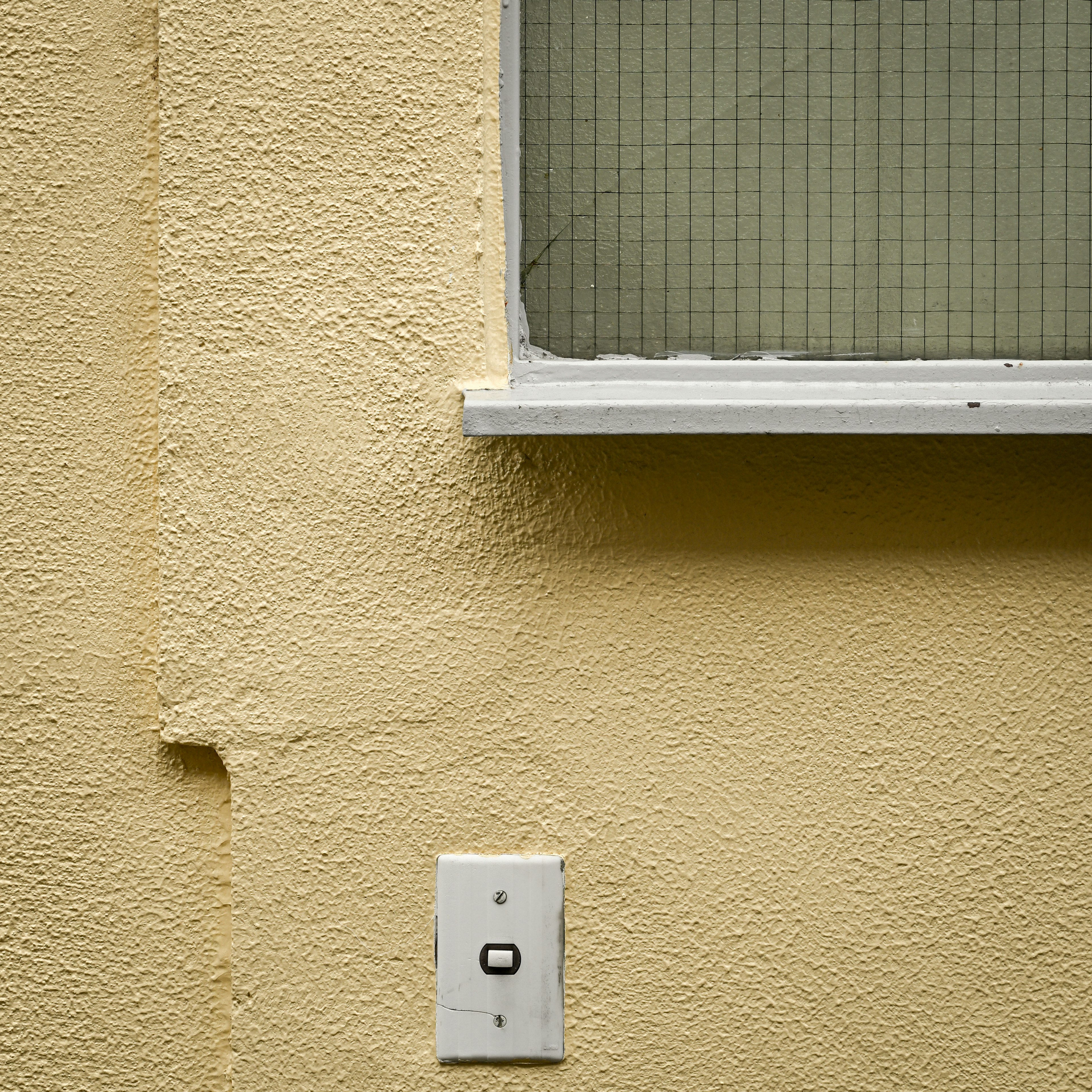 Composición simple de una pared amarilla con una ventana y un interruptor