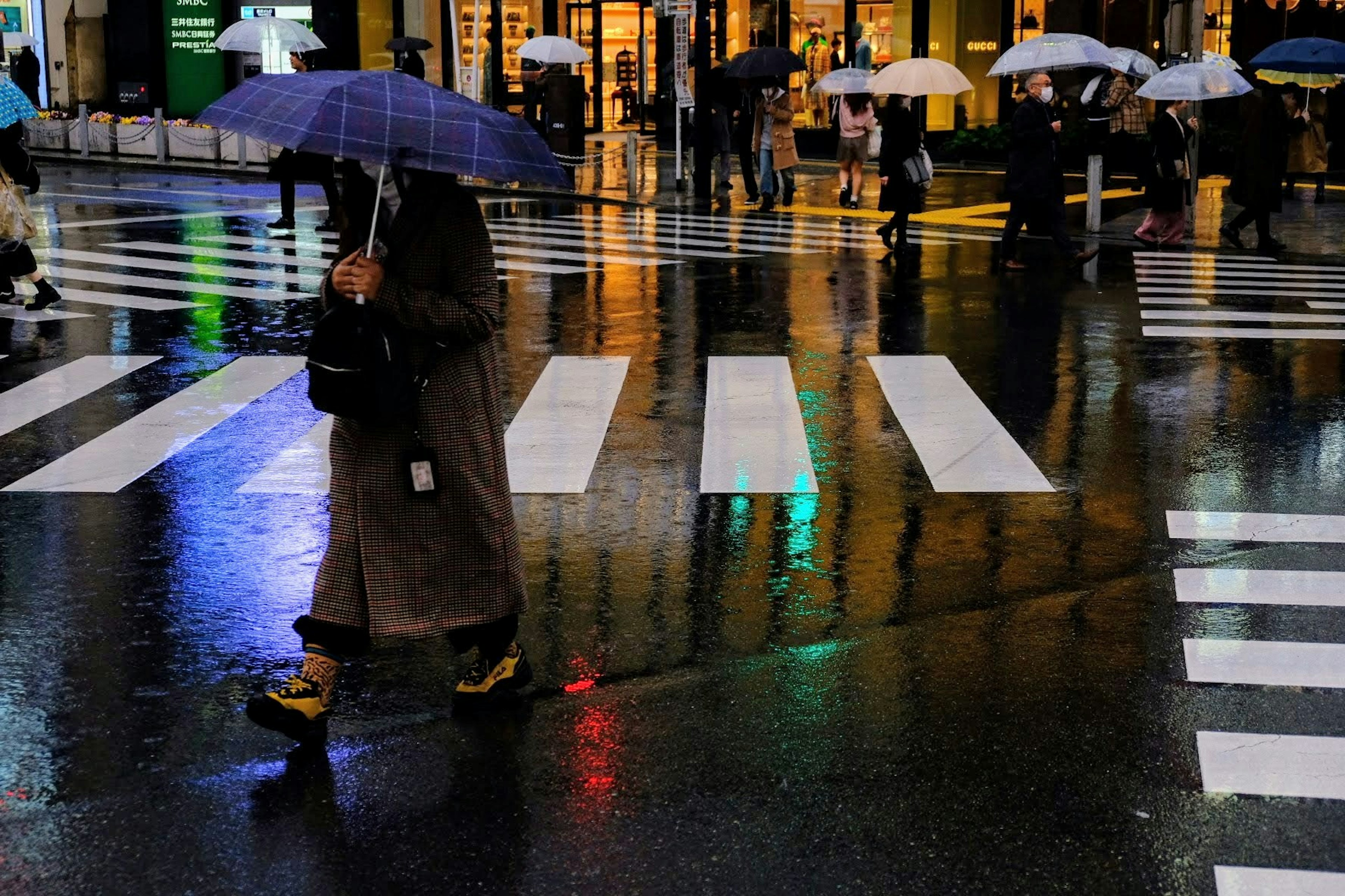 Persone con ombrelli che attraversano una strada sotto la pioggia Riflessi su un pavimento bagnato