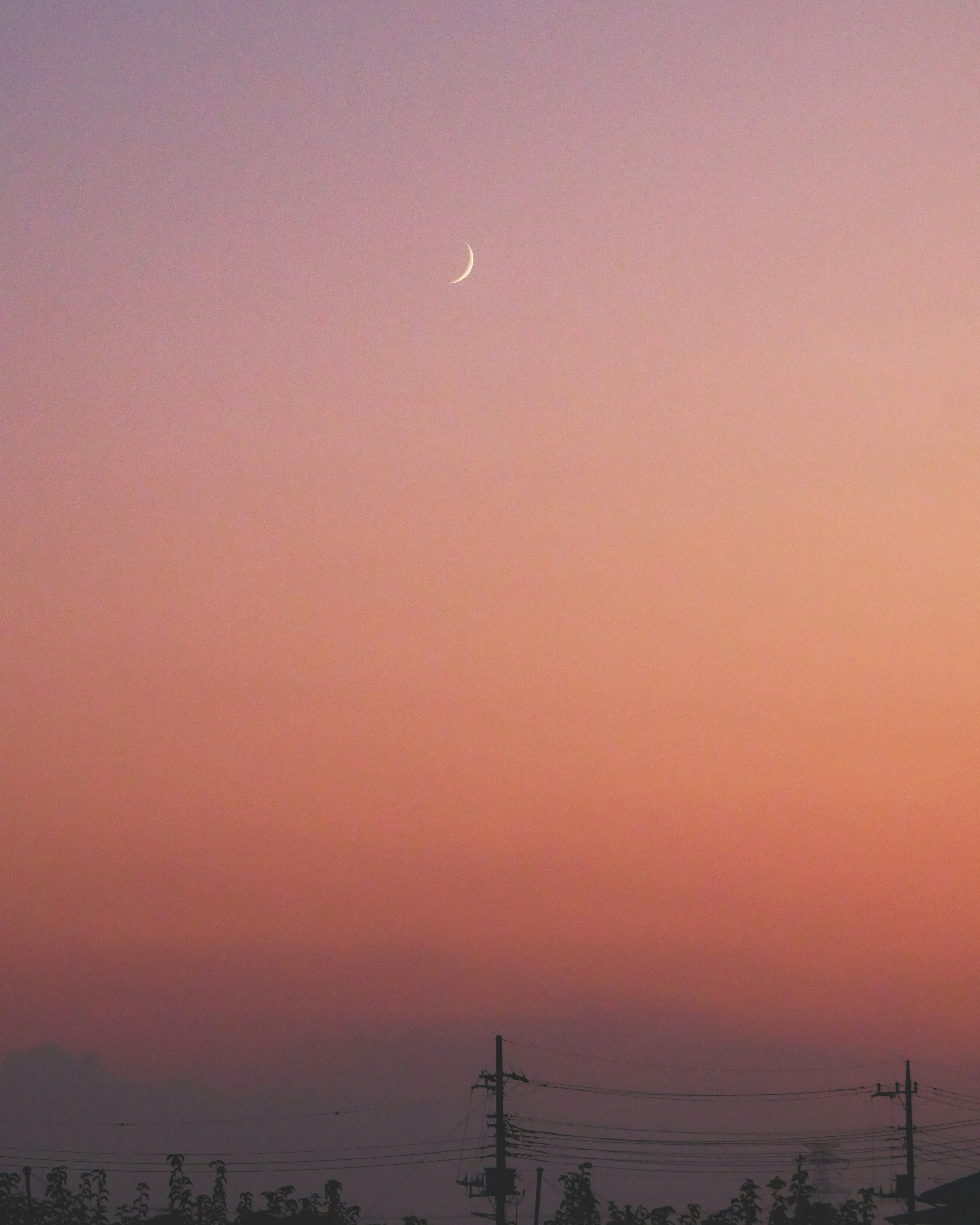 Bulan sabit tipis di langit gradasi oranye dan ungu