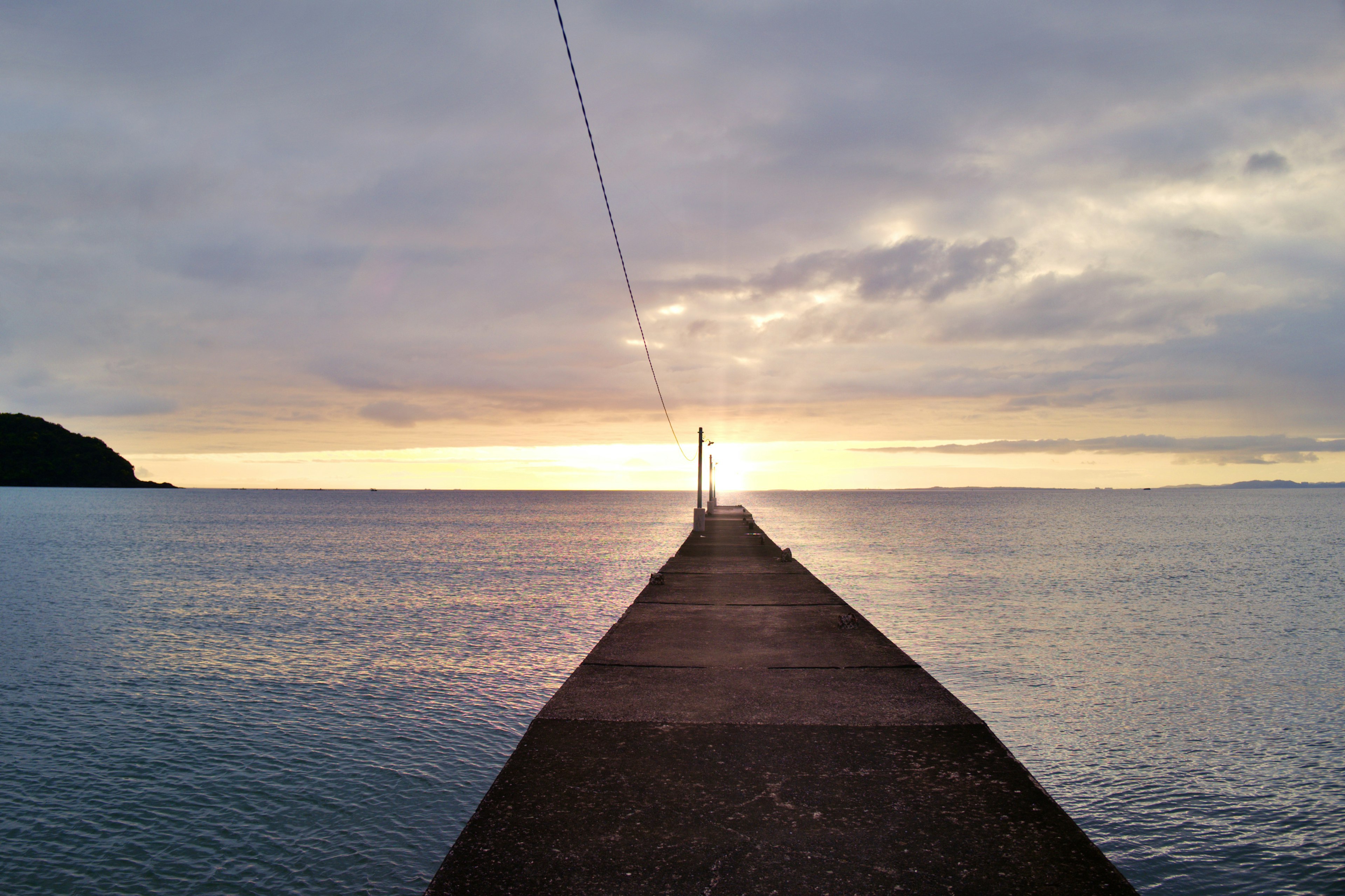 Molo che si estende nel mare con un faro al tramonto