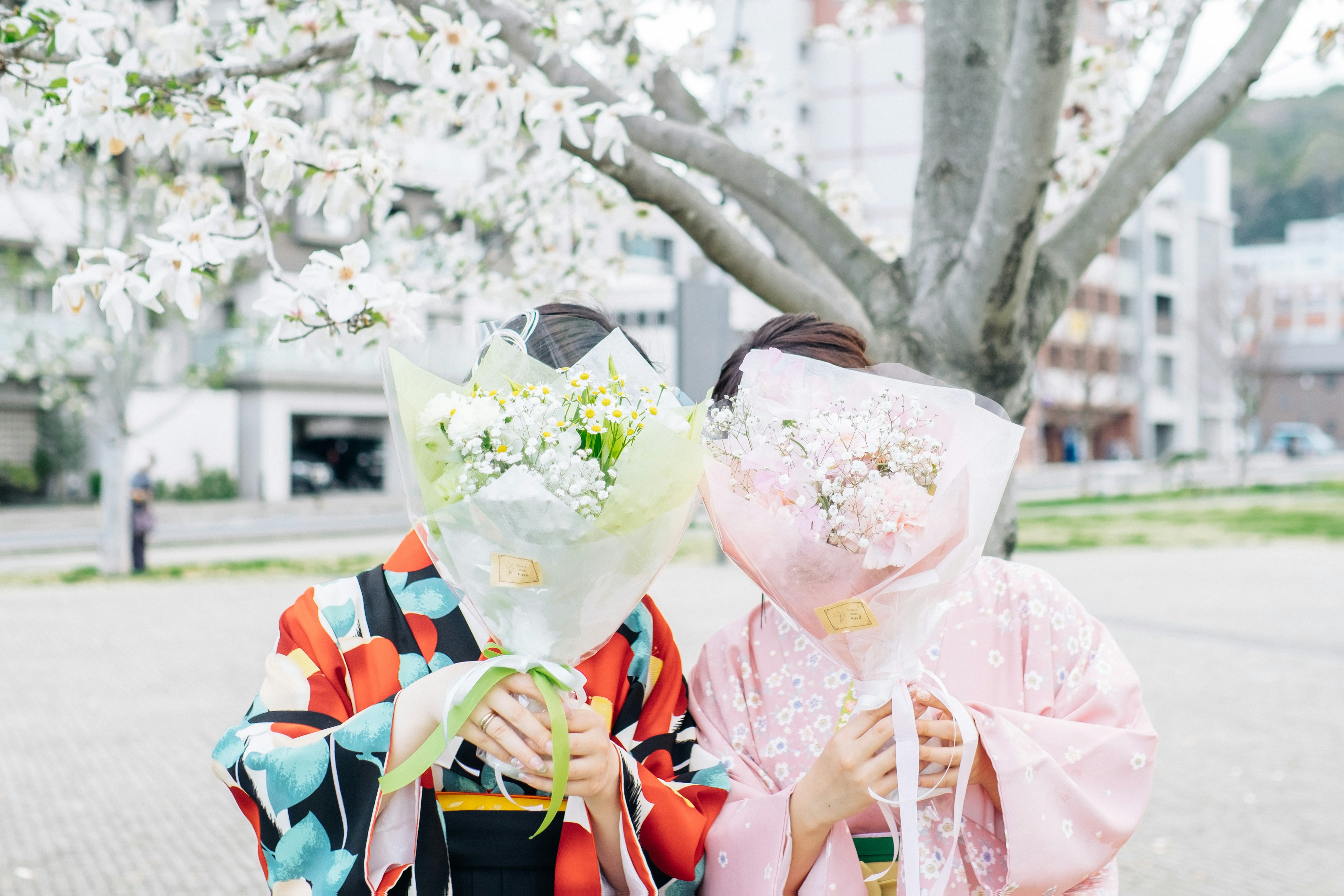 二人の女性が花束を持ち桜の木の下でポーズを取る