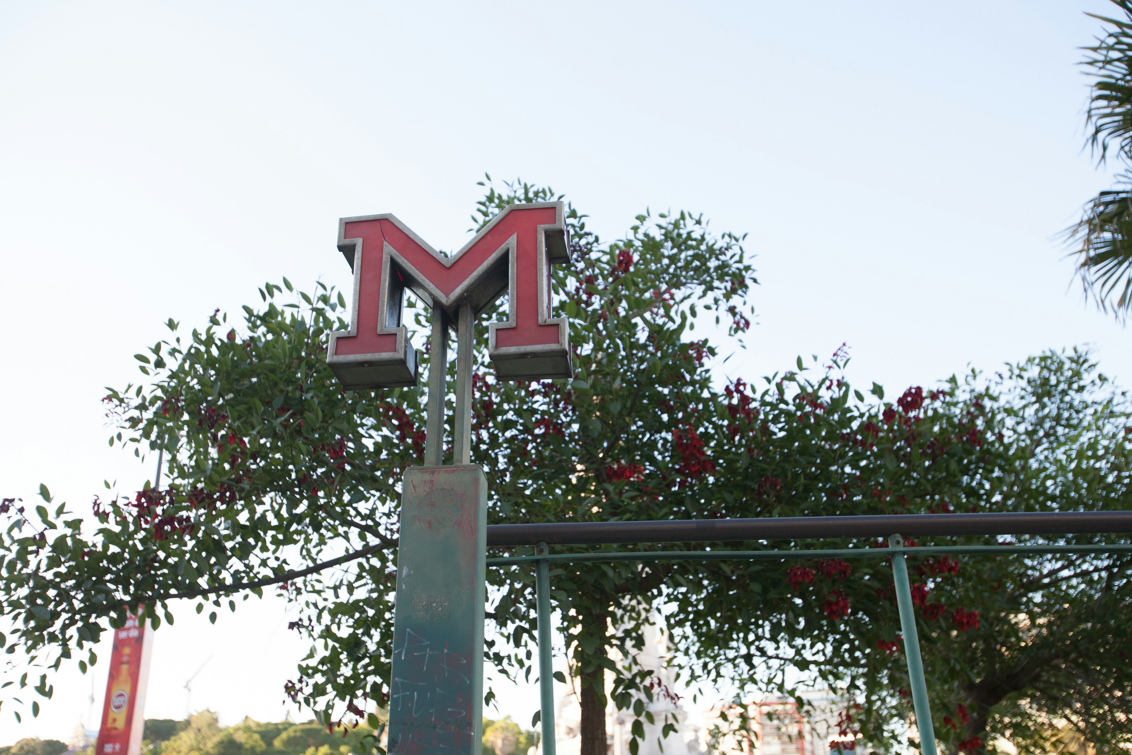 Landscape featuring a red M logo with flowers and trees in the background