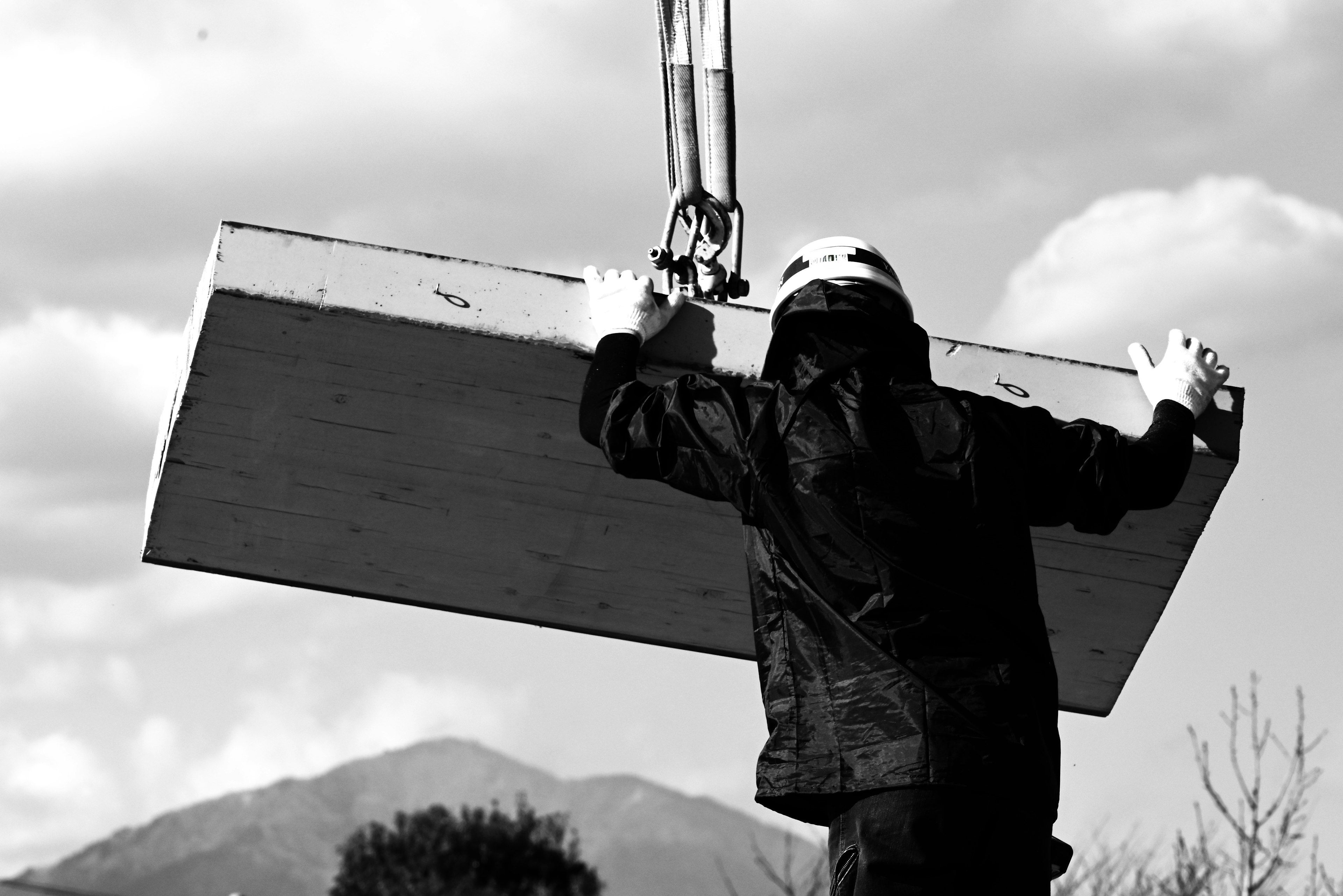 Worker in black and white attire holding a board lifted by a crane