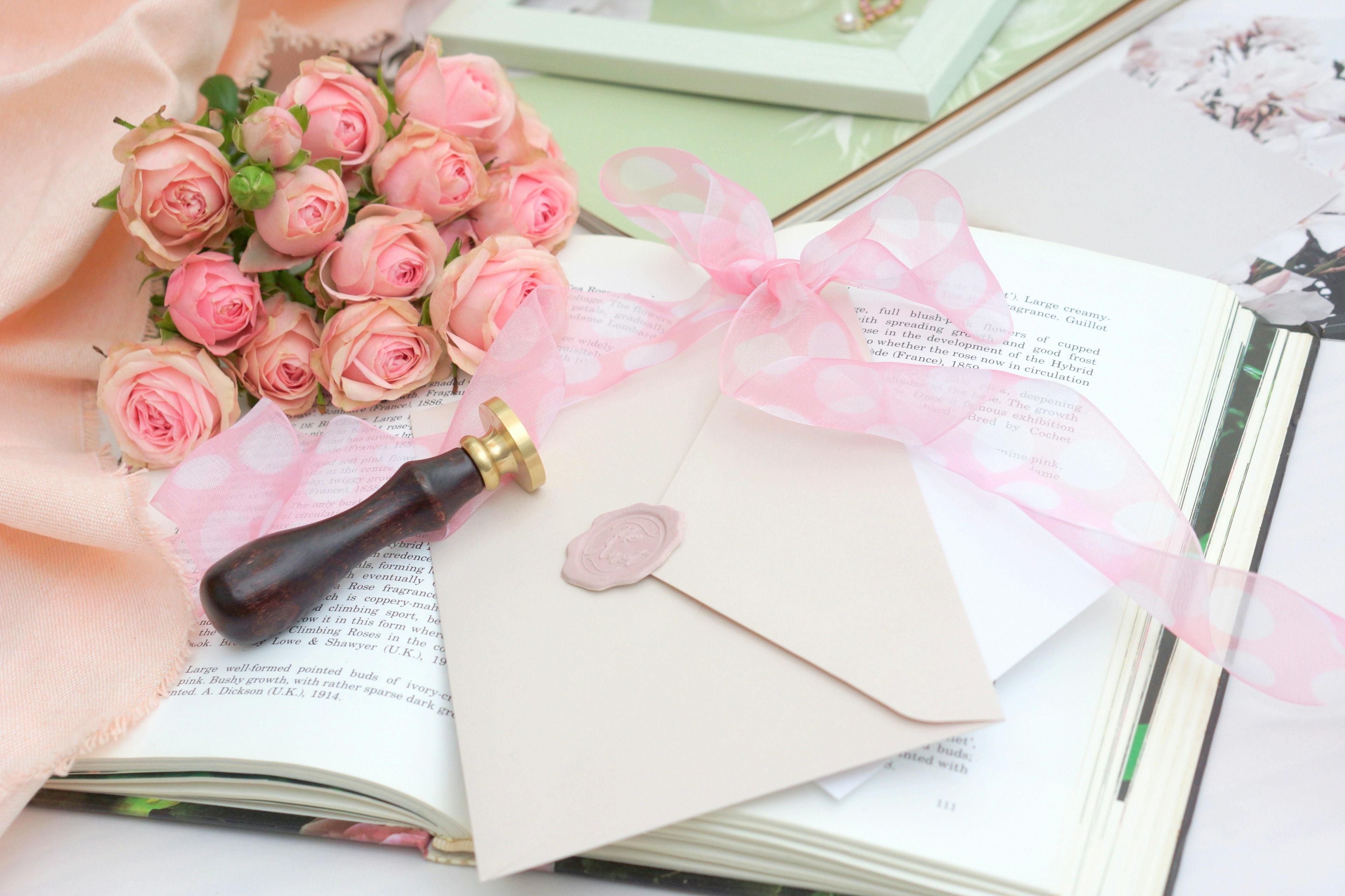 A beautiful still life featuring a bouquet of pink roses, a letter with a seal, and a ribbon