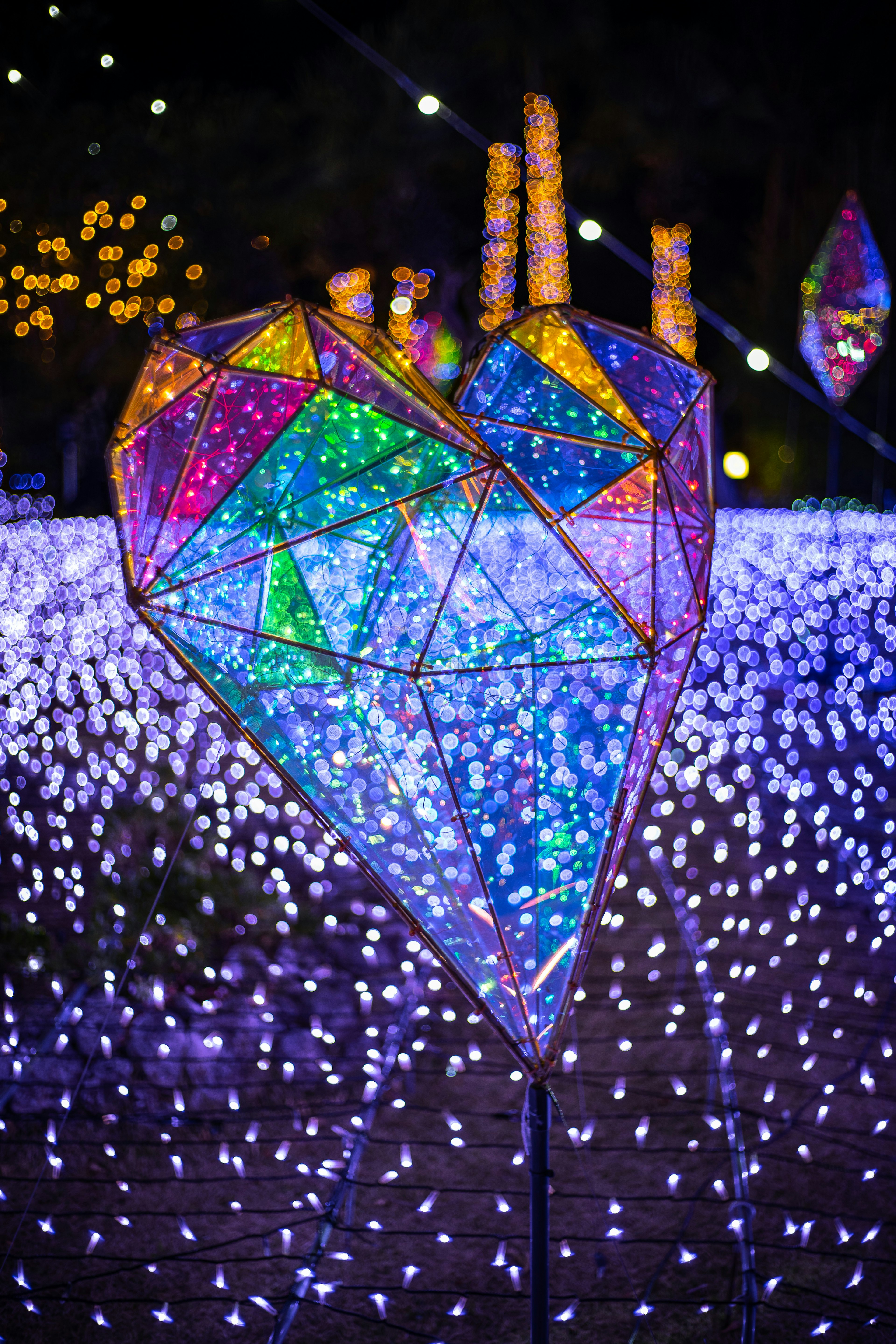 A heart-shaped light sculpture radiating colorful lights in a night setting