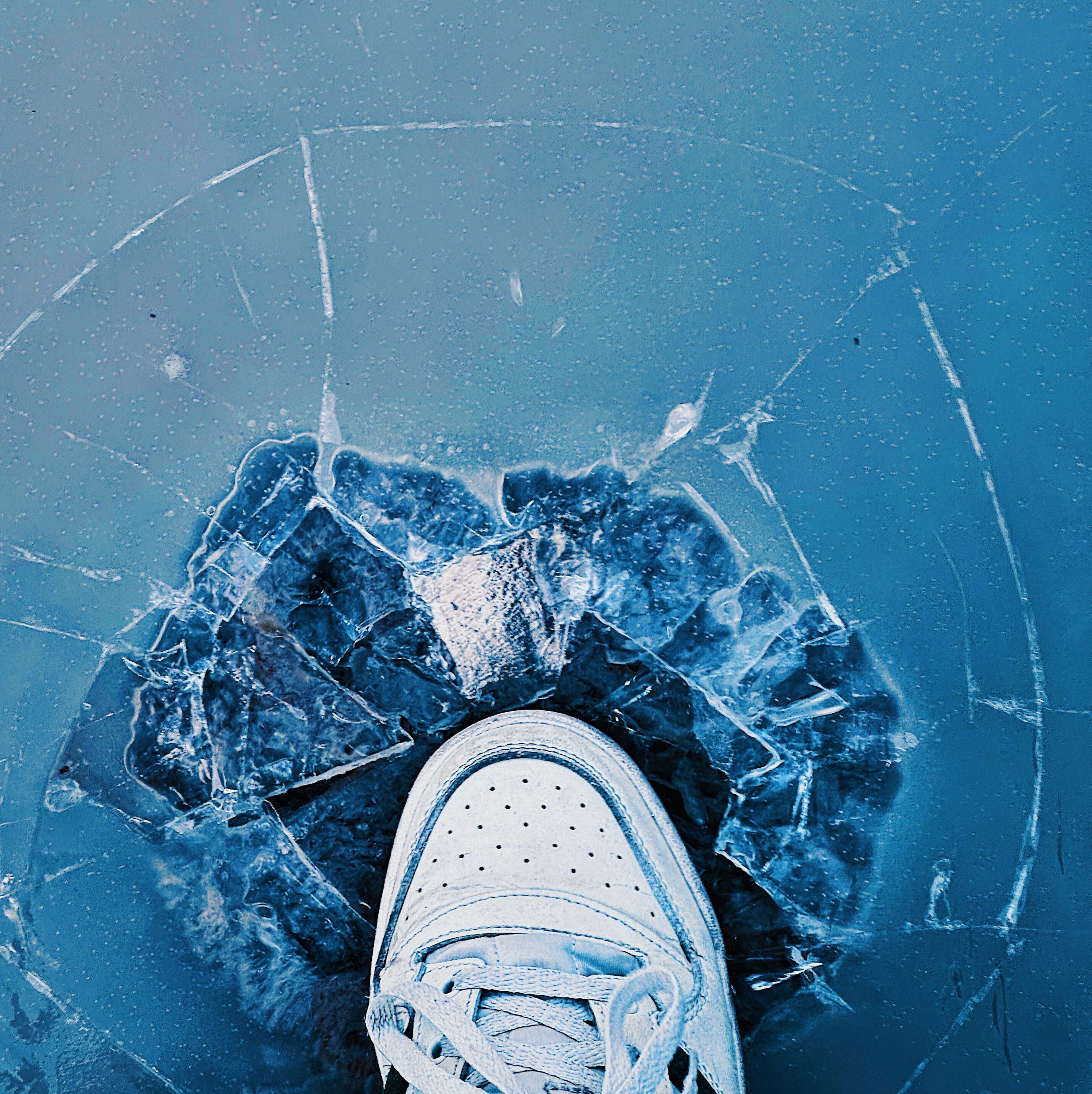 White sneaker standing on cracked ice with a blue background