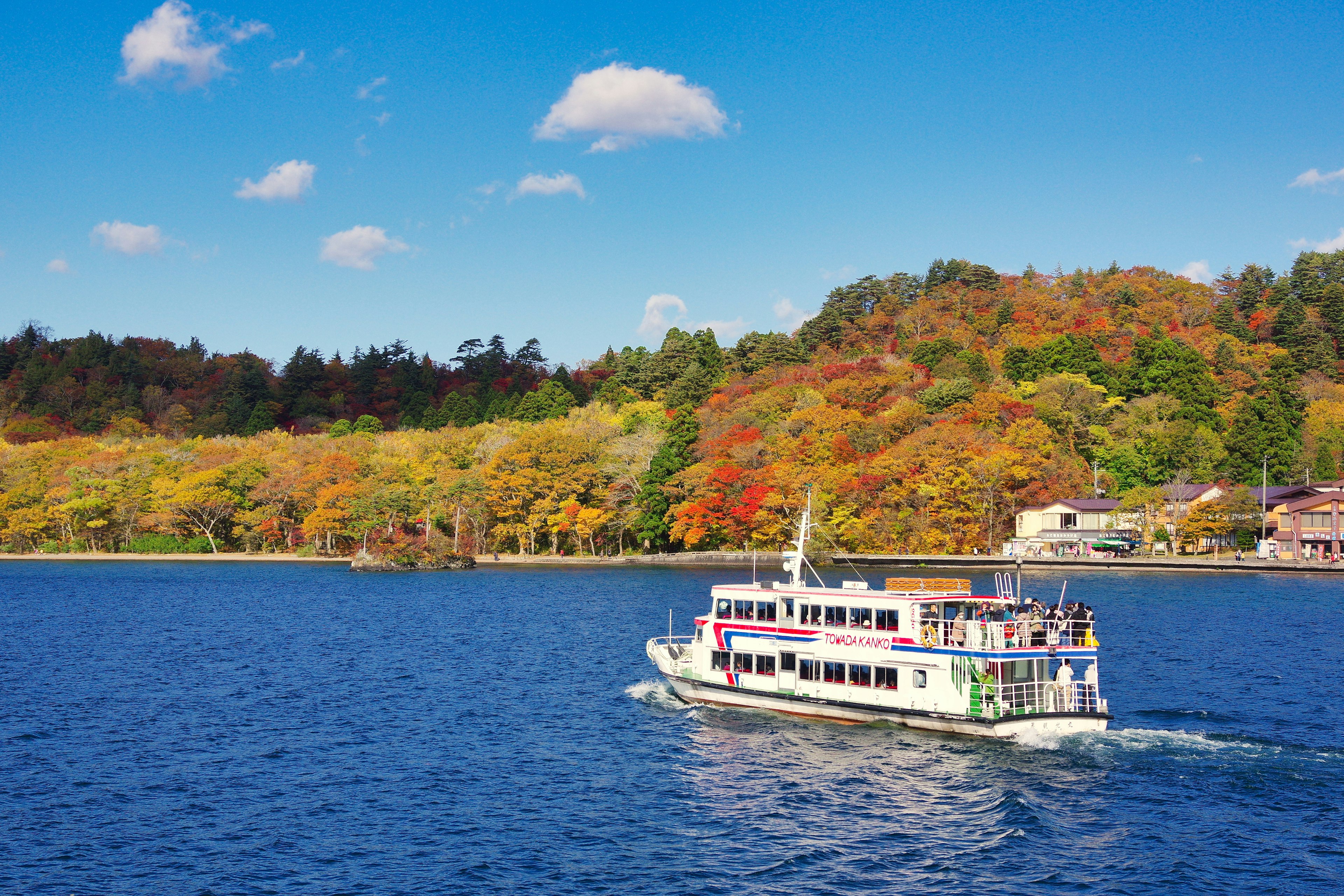 Touristenboot, das auf einem blauen See mit Herbstlaub fährt