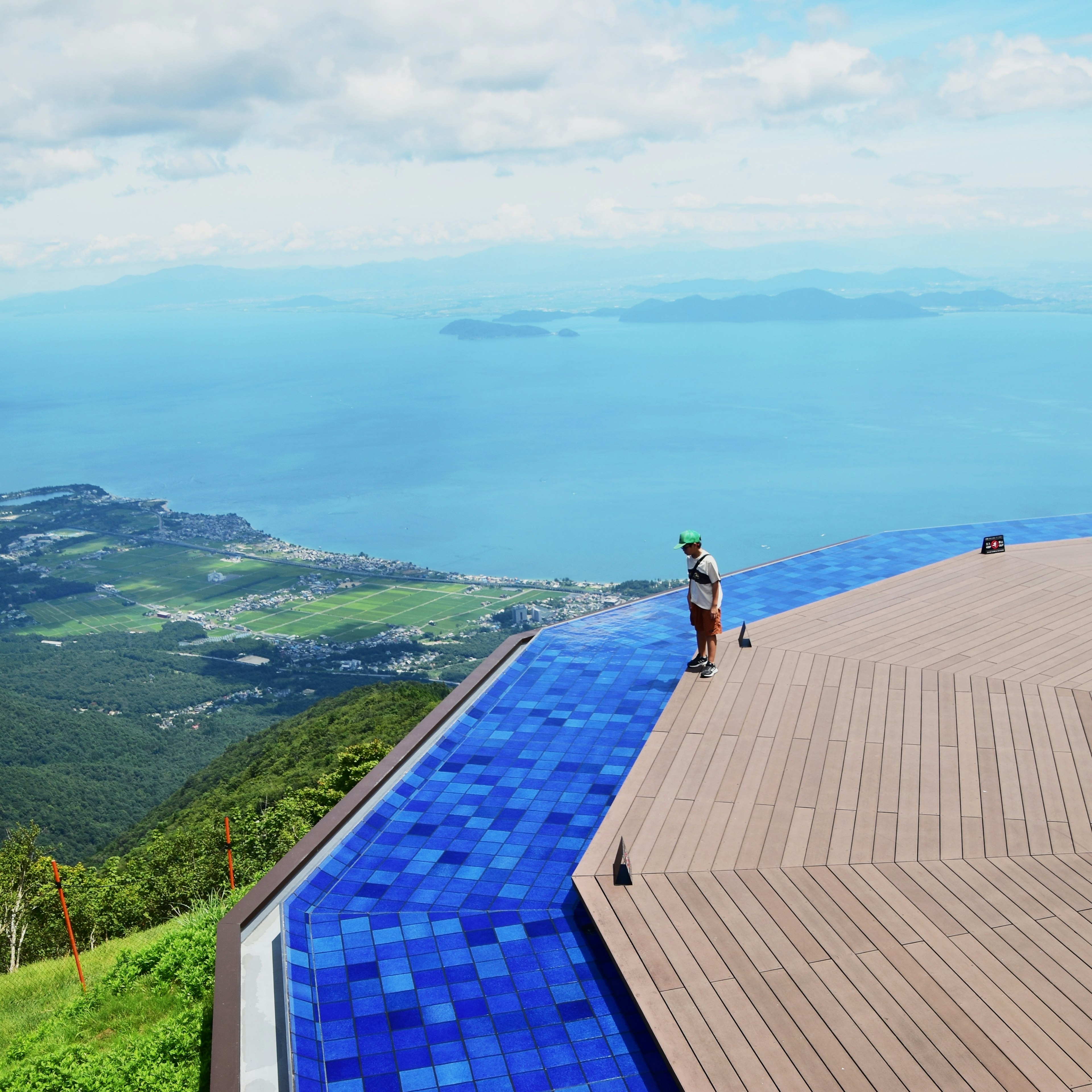 Person steht an einem blauen Infinity-Pool mit Blick auf den Ozean