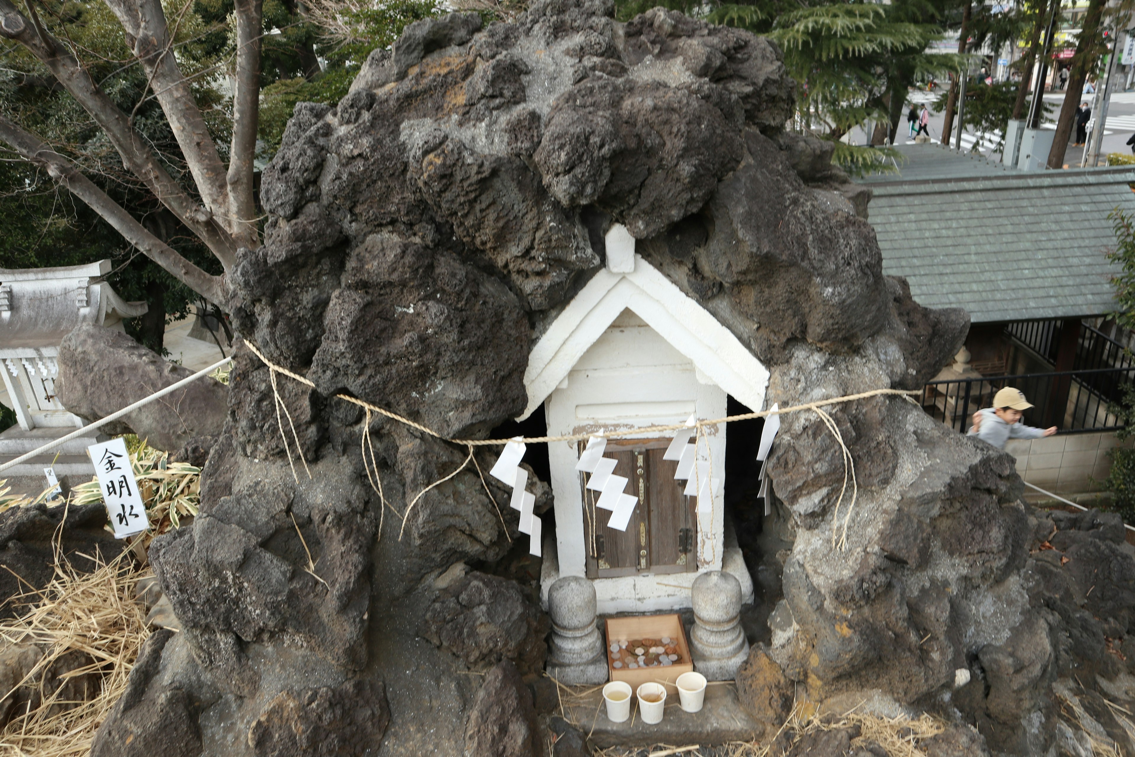 Un petit sanctuaire construit dans une roche volcanique sombre avec une structure blanche et des offrandes visibles