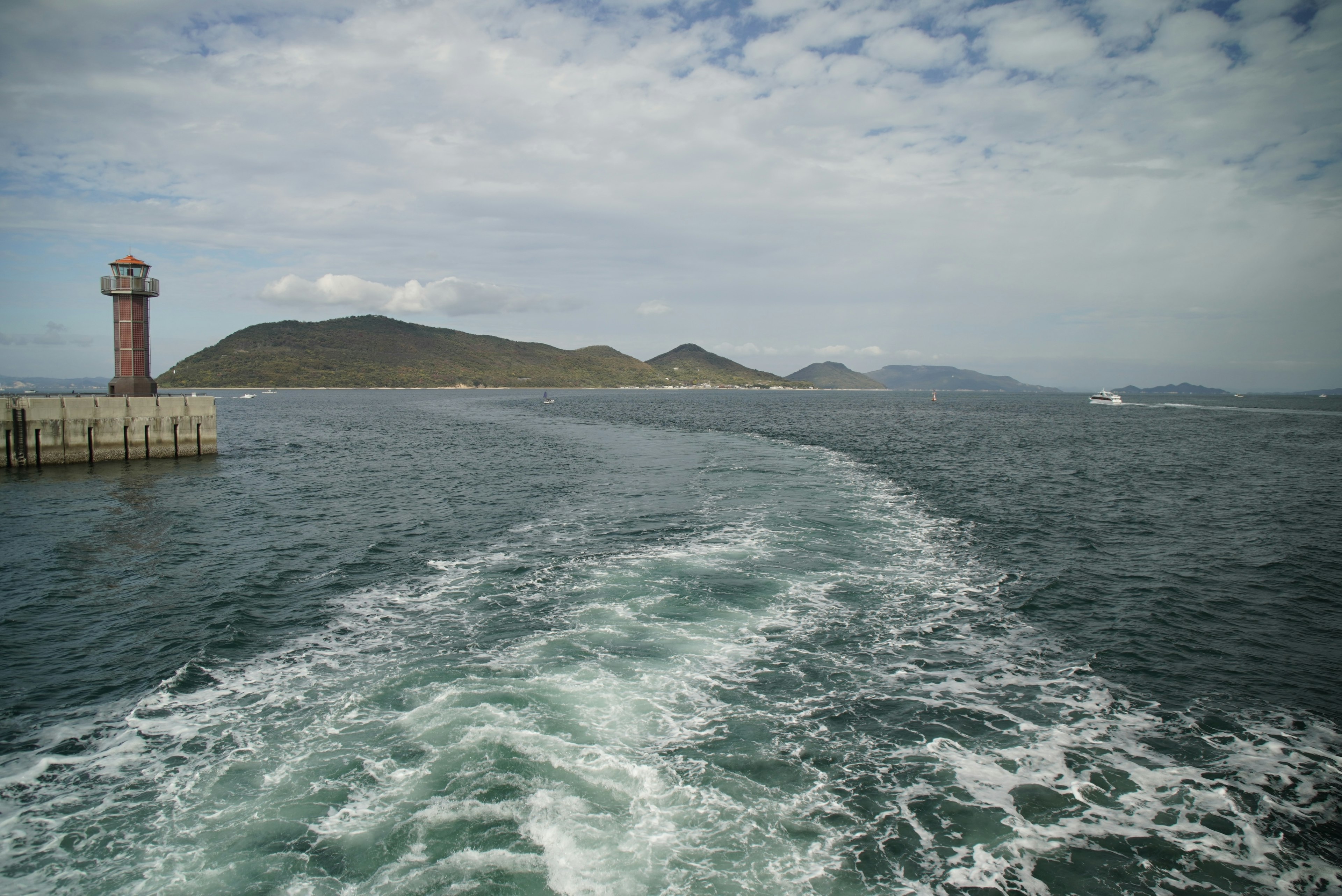 Escena costera con un faro y estela de barco