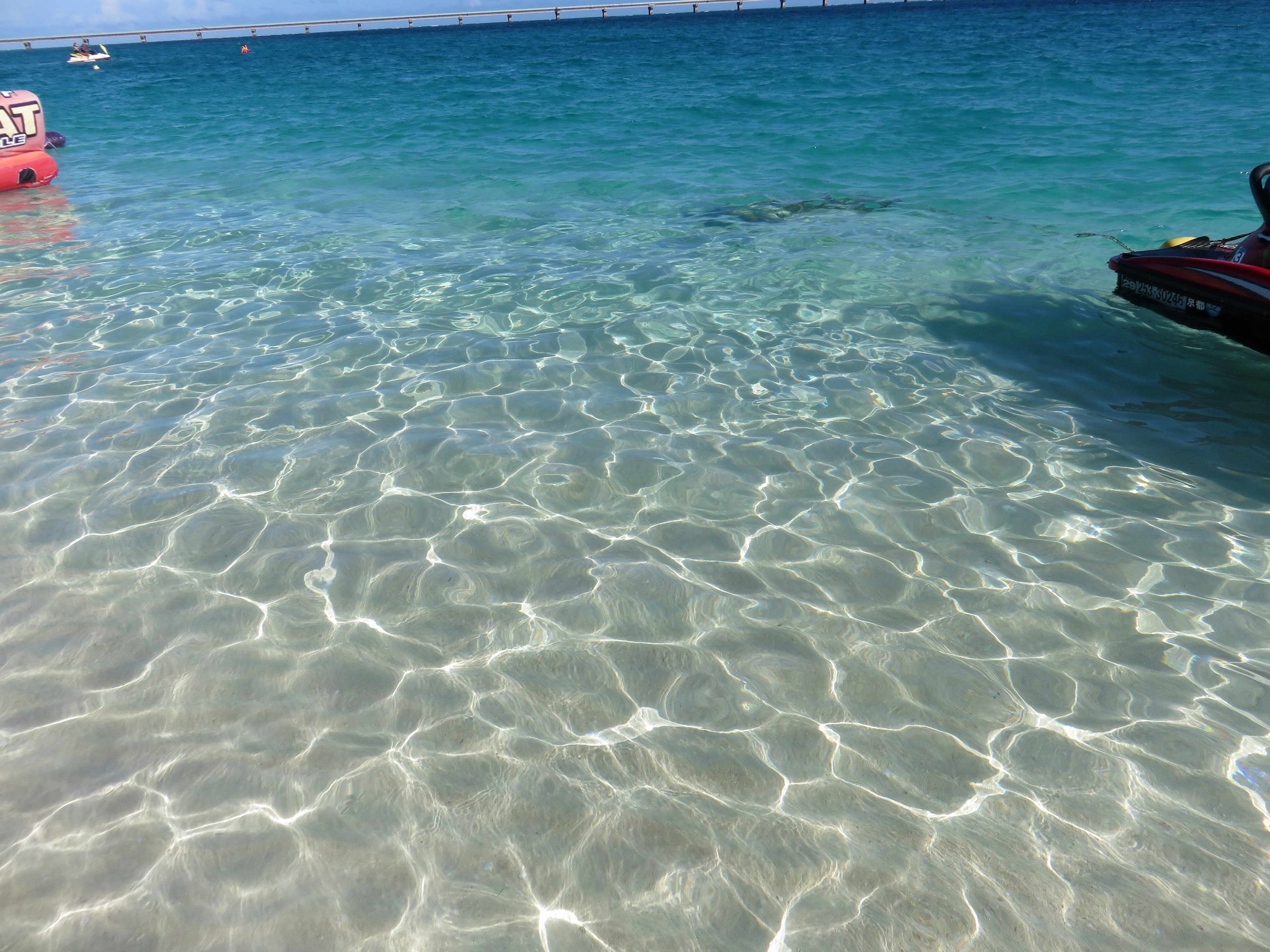 Air laut turquoise jernih dengan pantulan berkilau di pantai yang cerah