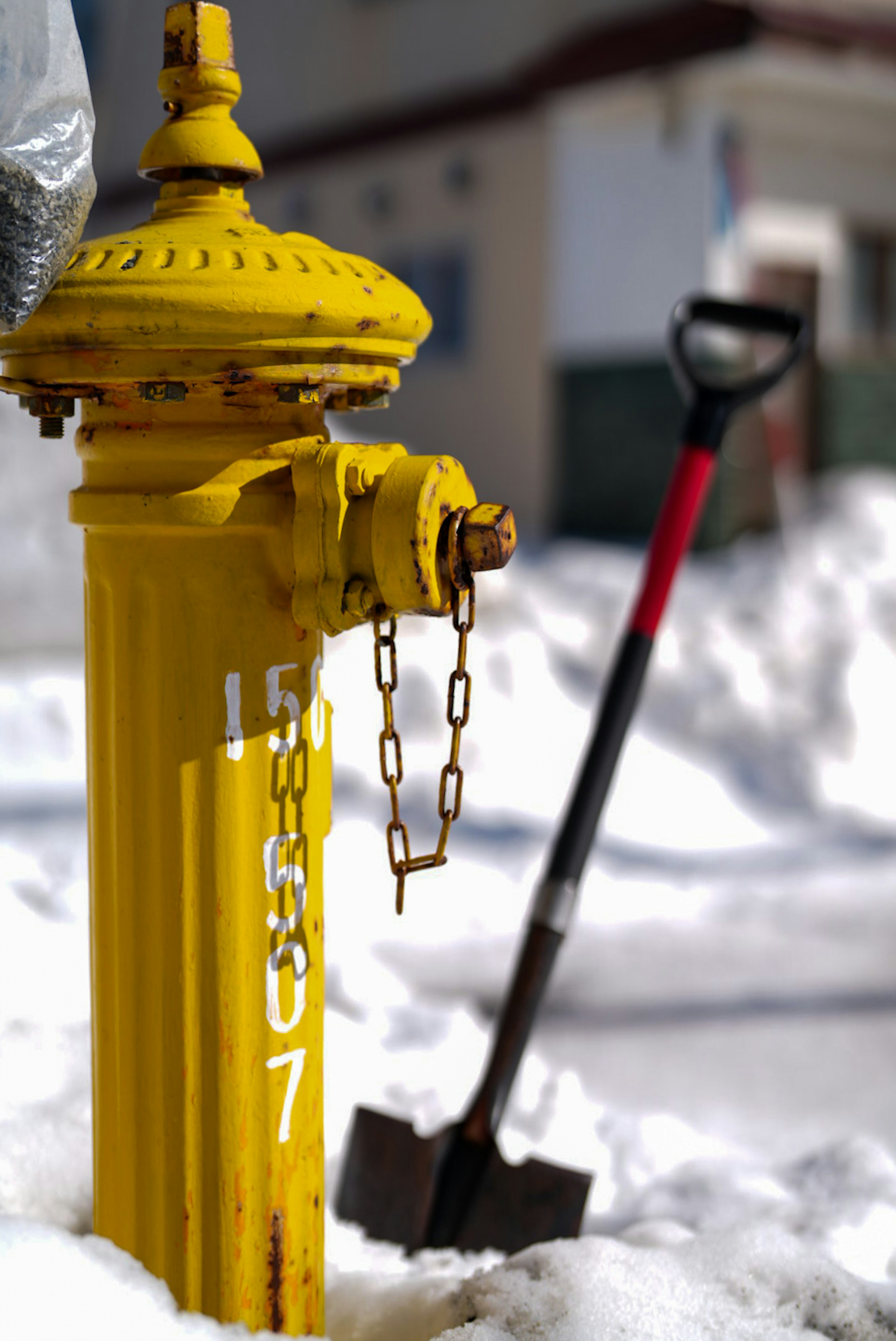 Yellow fire hydrant partially buried in snow with a shovel nearby