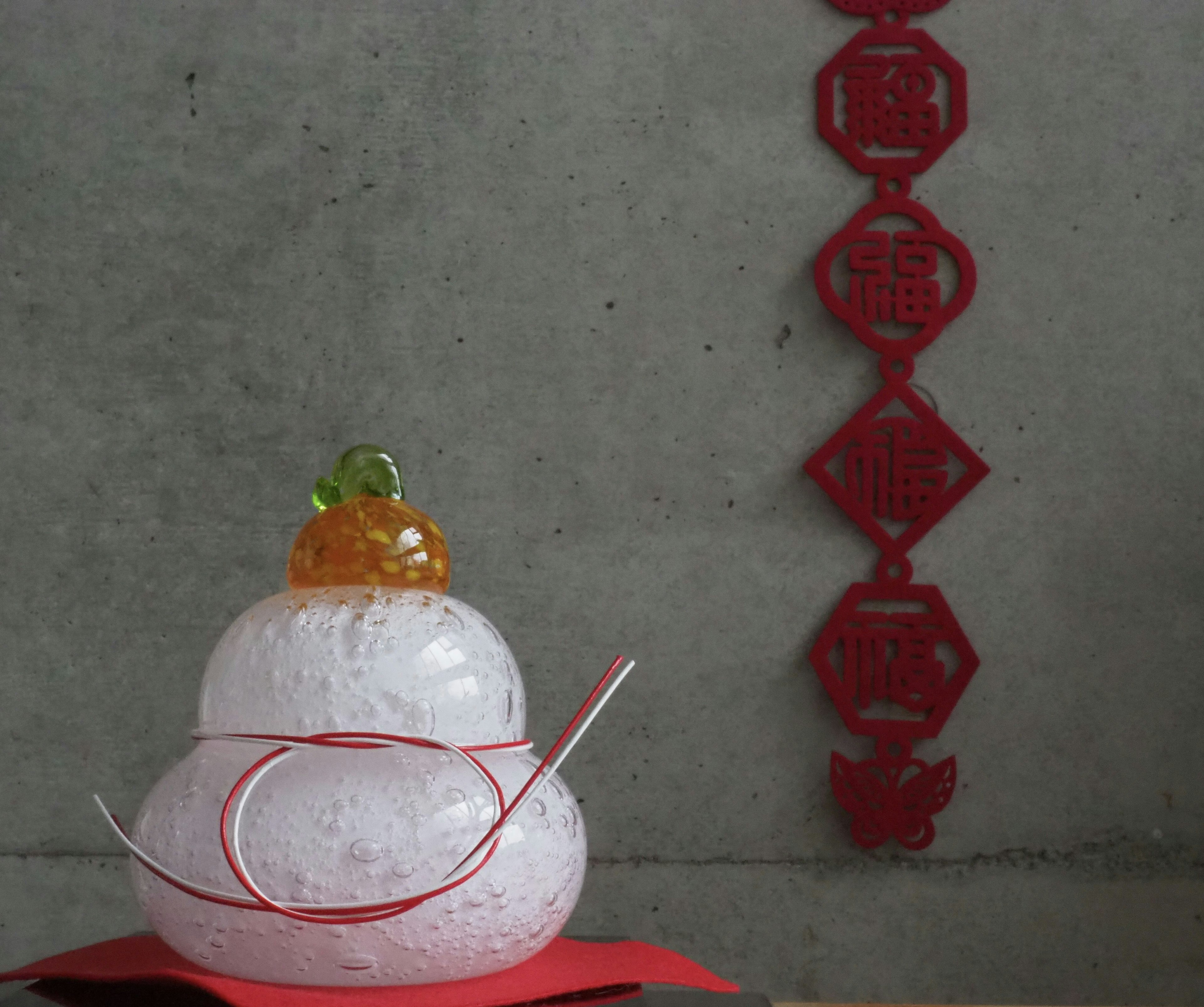 A decorative white round object topped with orange and green ornaments with red decorations in the background