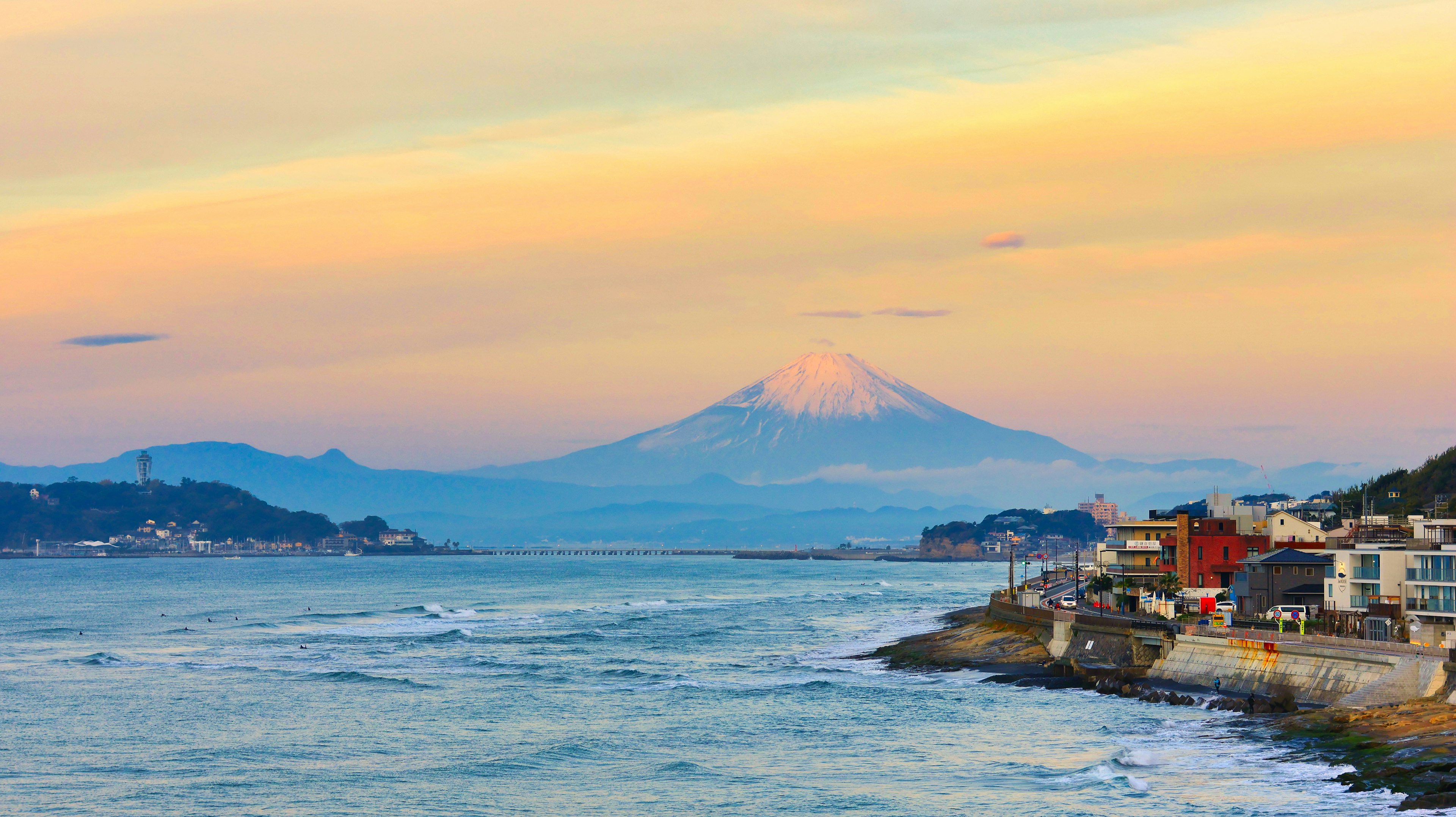 Scenic view of Mount Fuji at sunset with coastal buildings and ocean waves