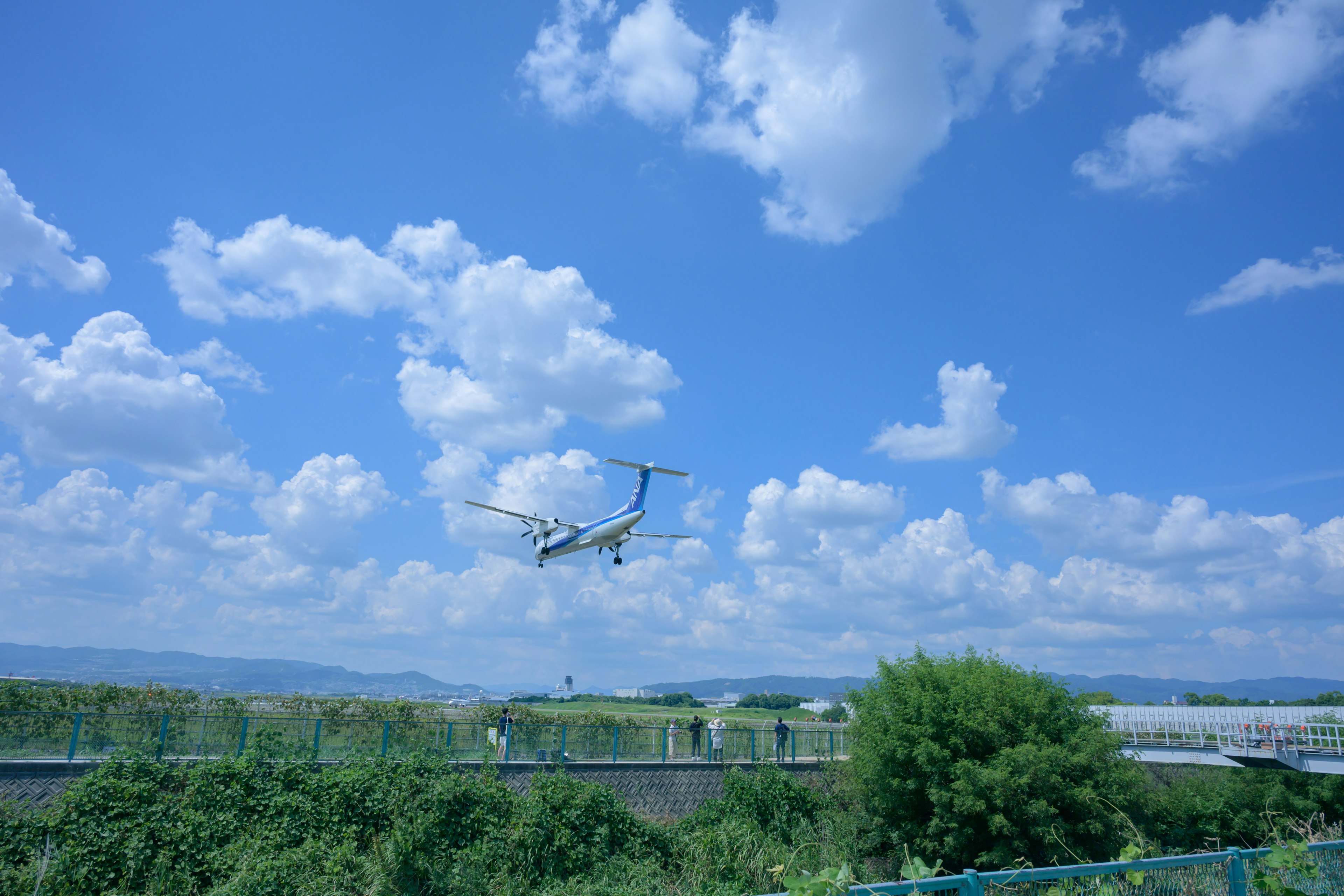 An airplane landing under a blue sky with fluffy clouds and green landscape