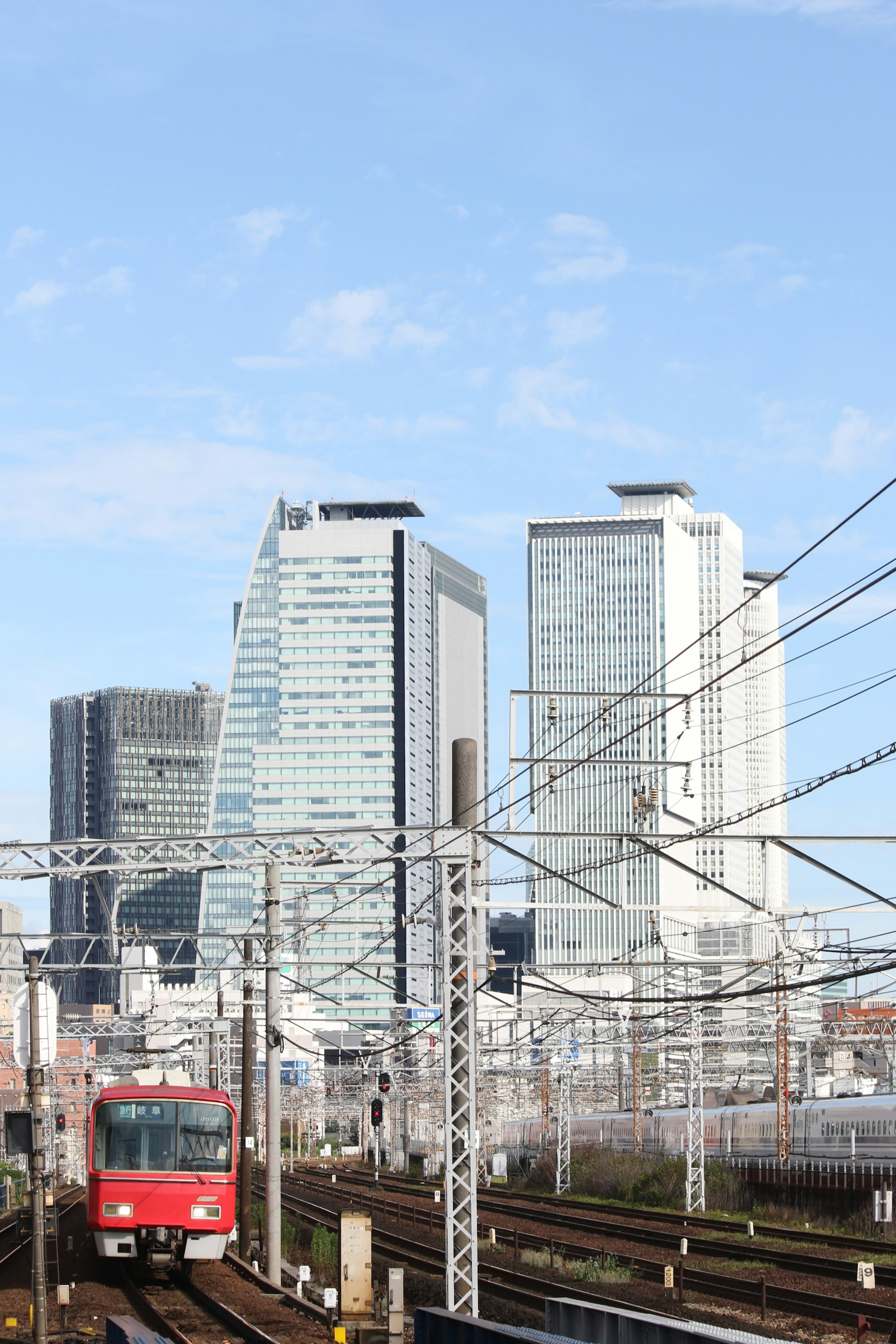 A red train runs along the tracks with skyscrapers in the background