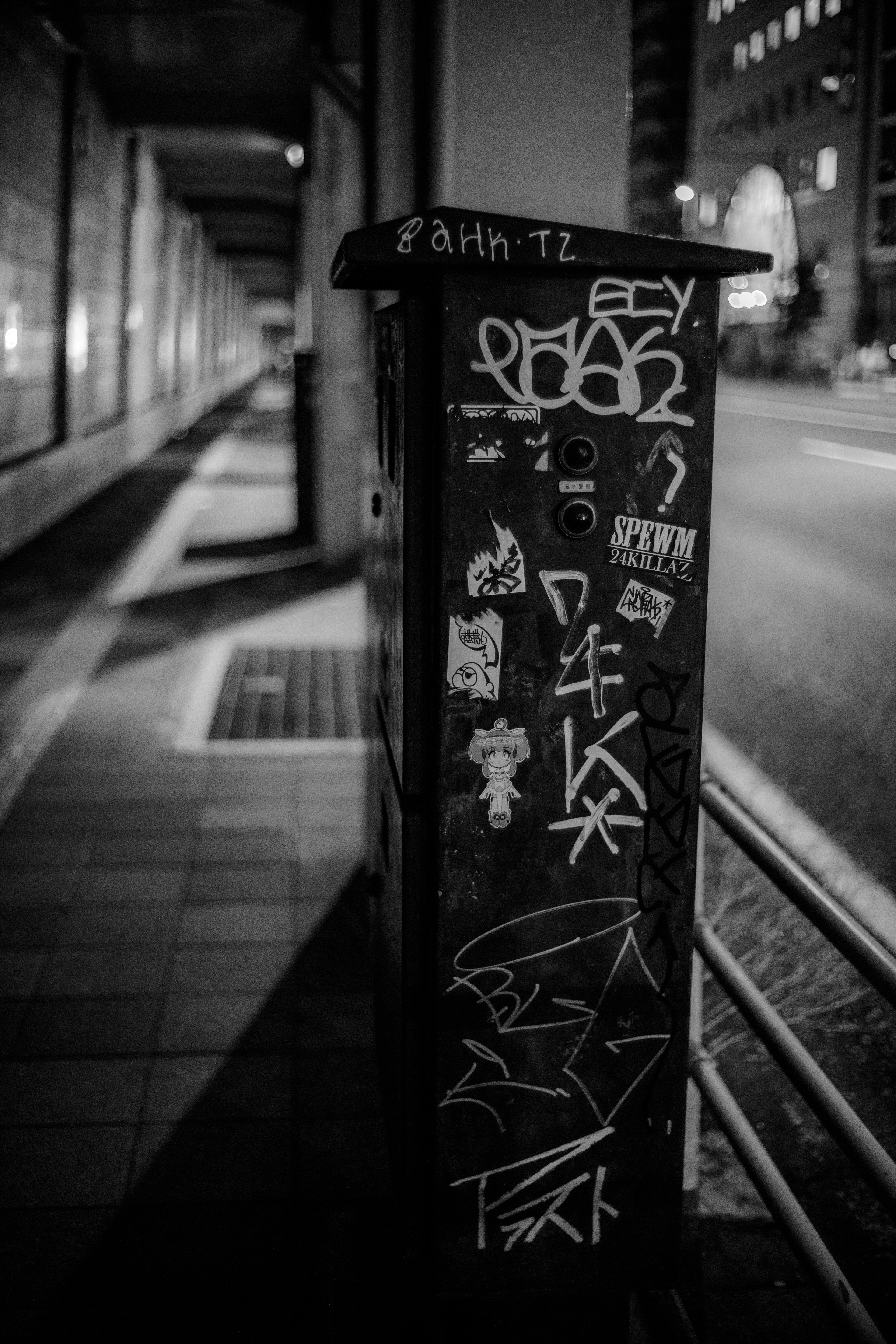 Black post covered in graffiti and stickers on a street corner at night